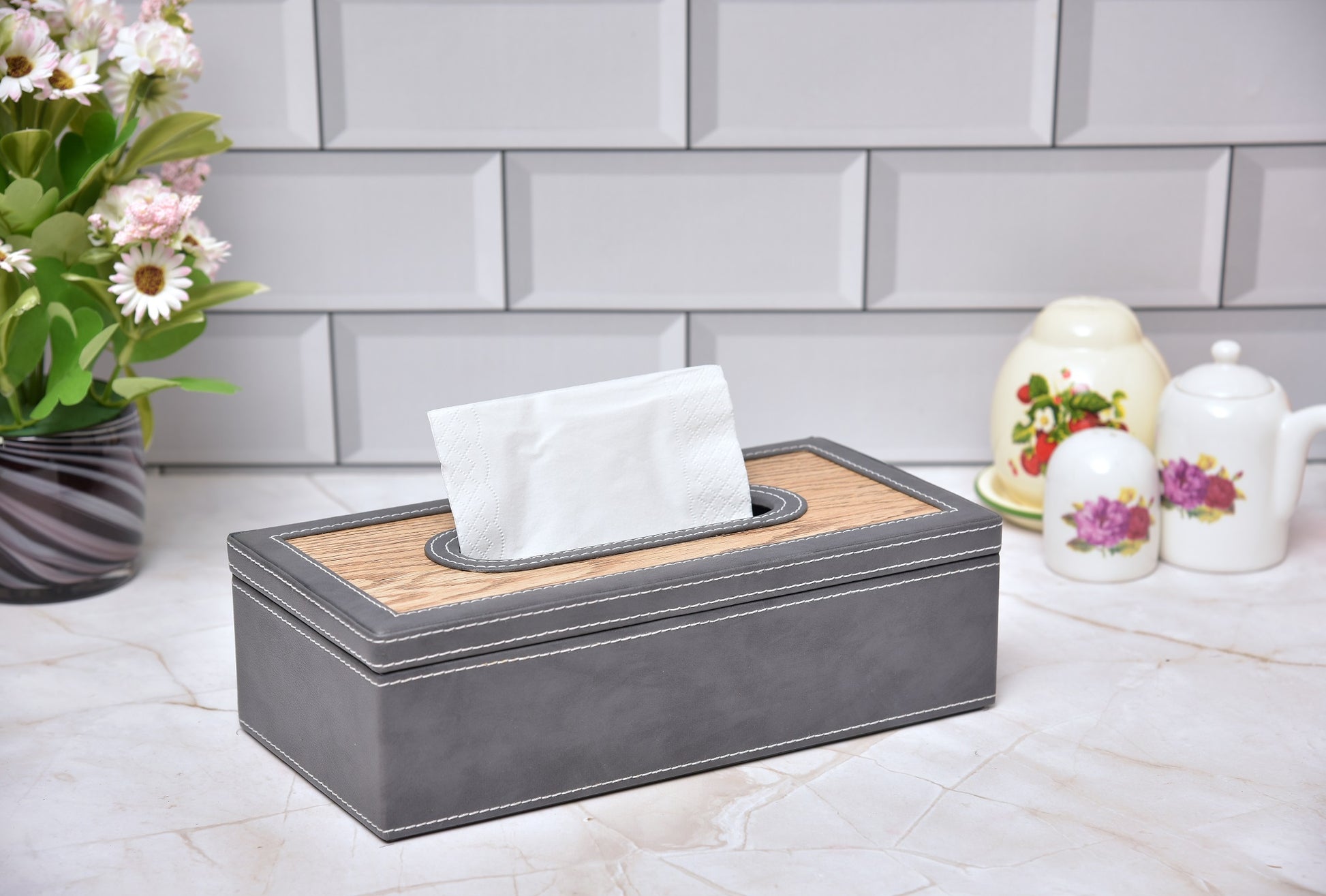 Rectangular tissue box holder with grey leatherette body and wooden-look top, tissue visible