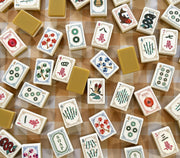 Mahjong tile set spread across the table with white faces and yellow backs