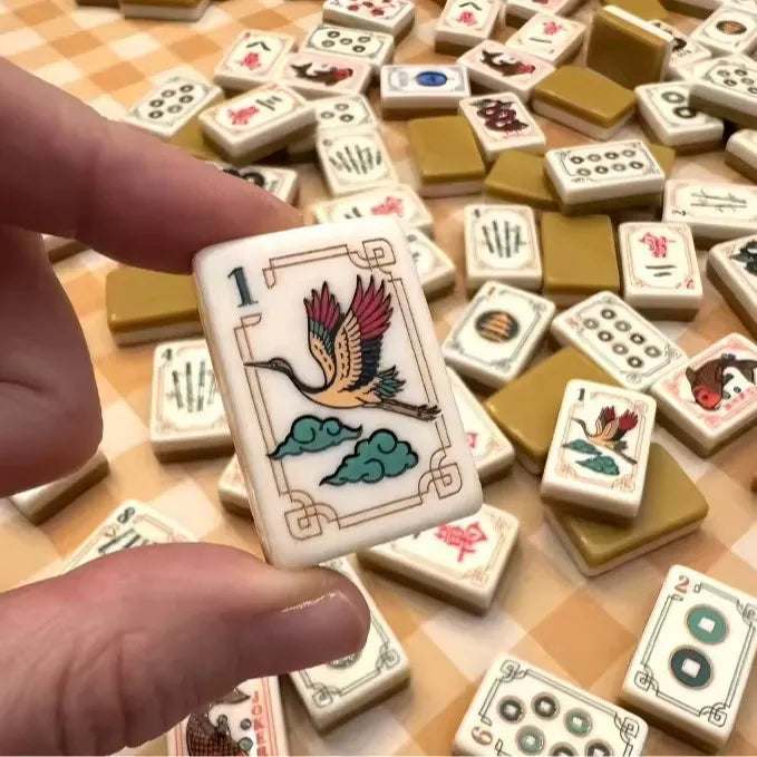 Hand holding a Mahjong tile with bird-and-cloud illustration among scattered tiles