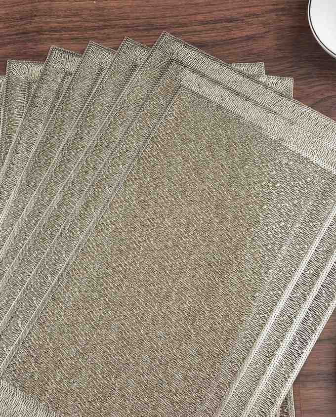 Stack of gold-toned vinyl rectangle placemats, textured finish with stitched edge border.