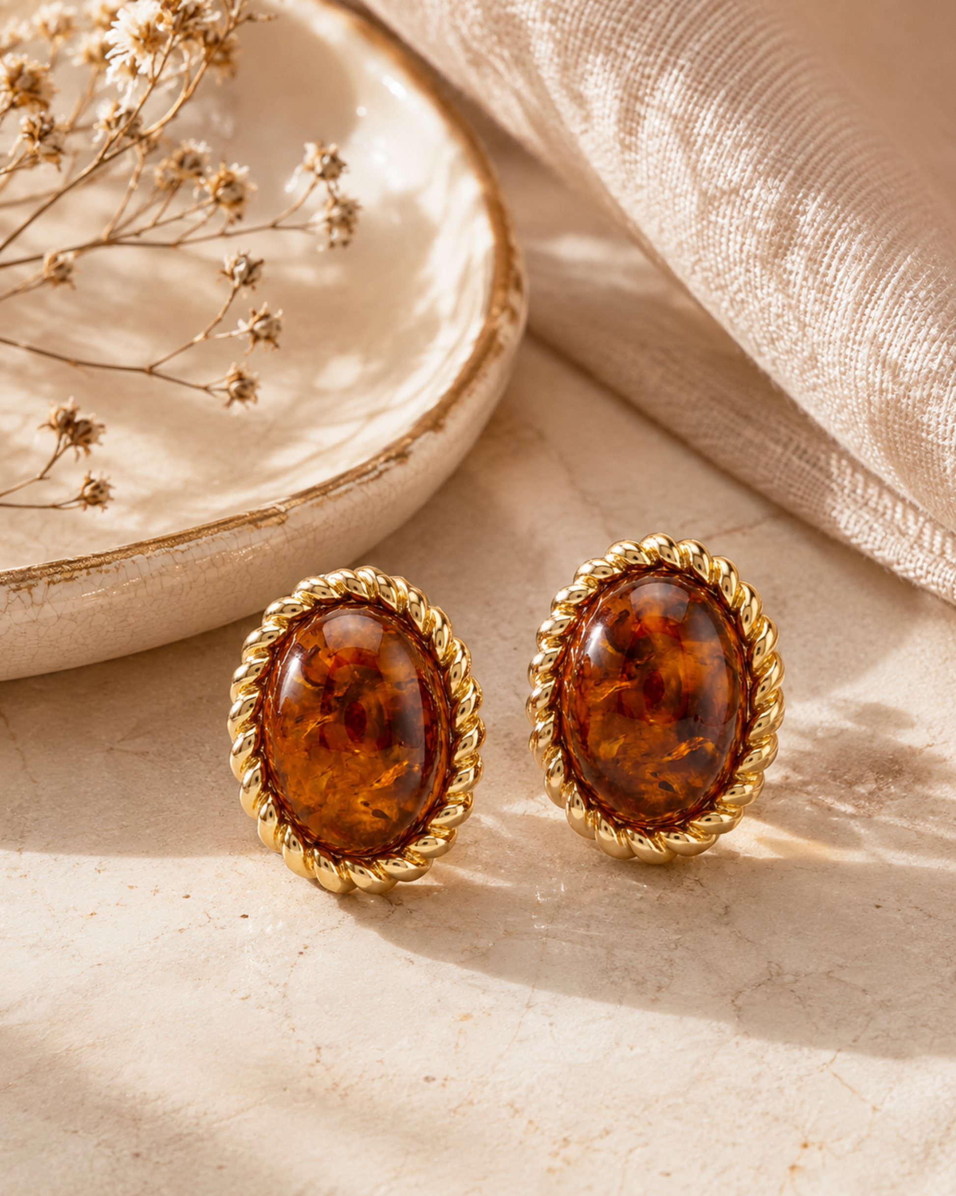 Pair of oval amber stud earrings with ornate gold-tone frame on tabletop