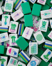 Close-up of mahjong tiles with white faces, green/blue stripes, and colorful plant and number symbols