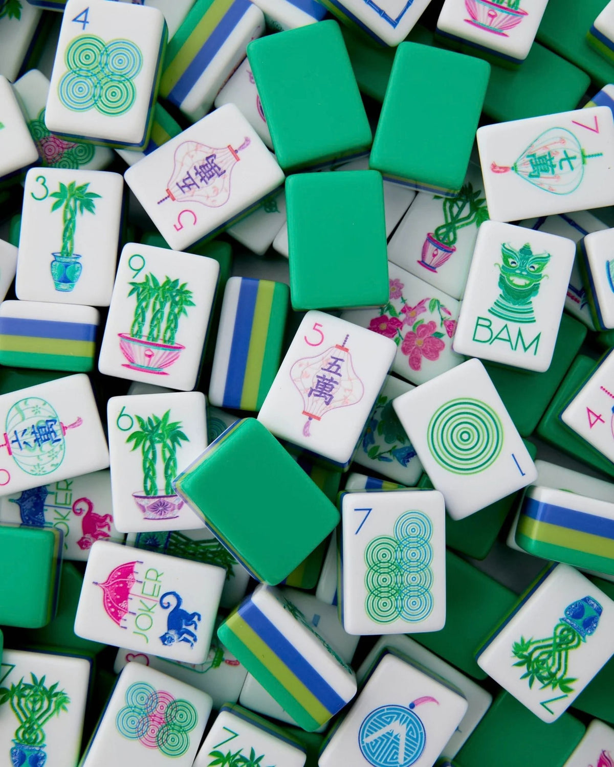 Close-up of mahjong tiles with white faces, green/blue stripes, and colorful plant and number symbols