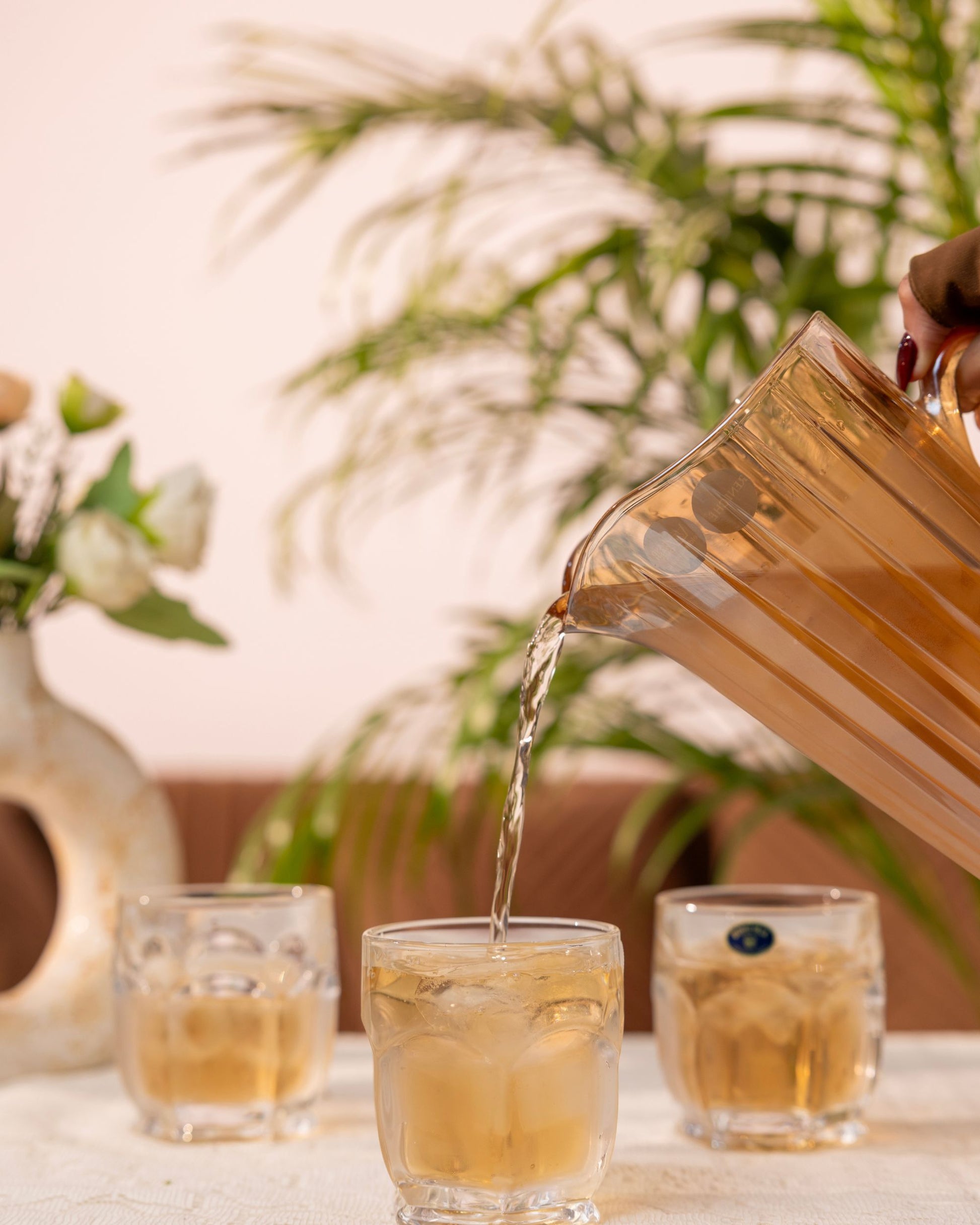 Amber glass water jug pouring into faceted crystal tumbler, with two other tumblers