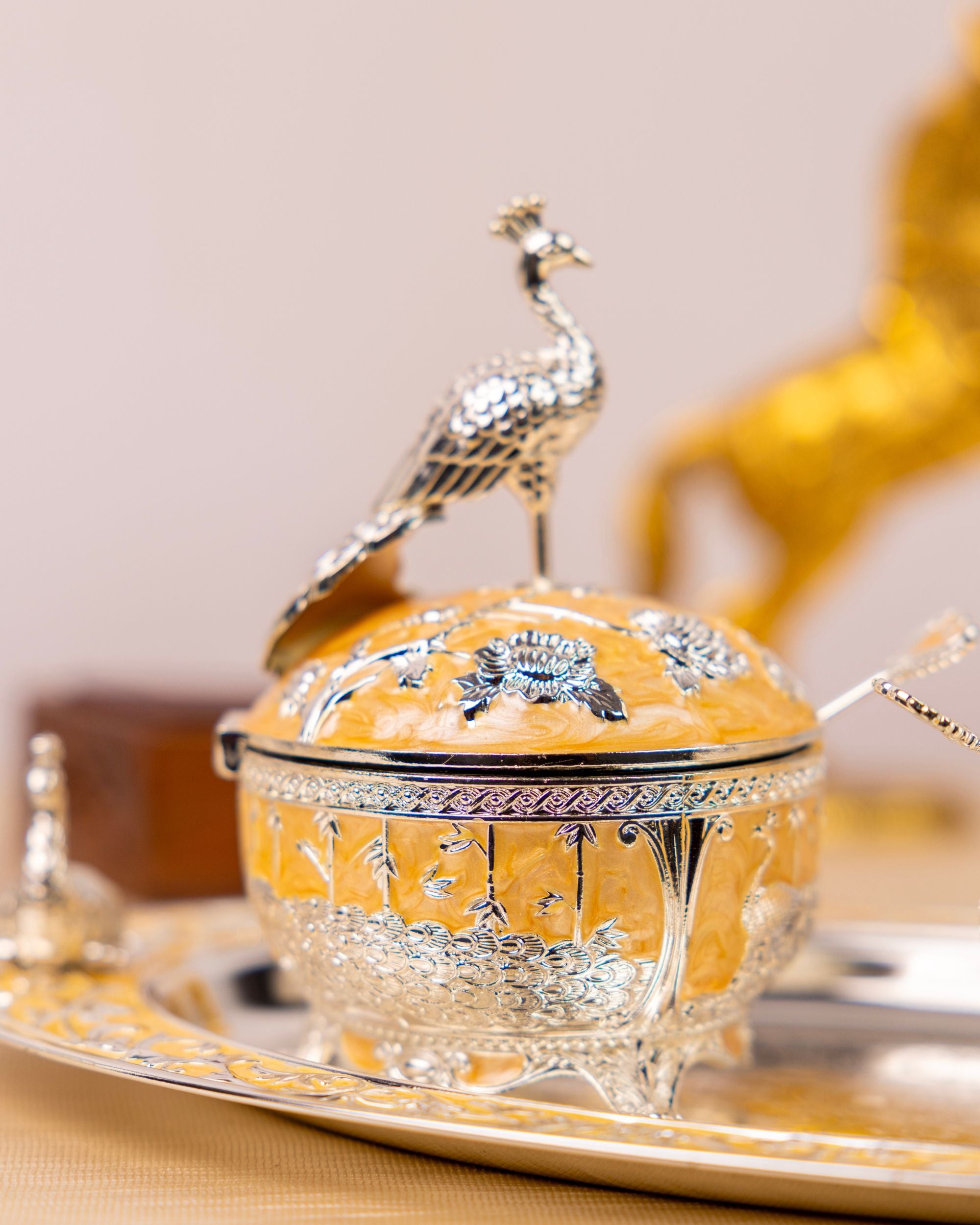 Covered serving bowl with peacock finial, set on ornate gold-and-silver tray