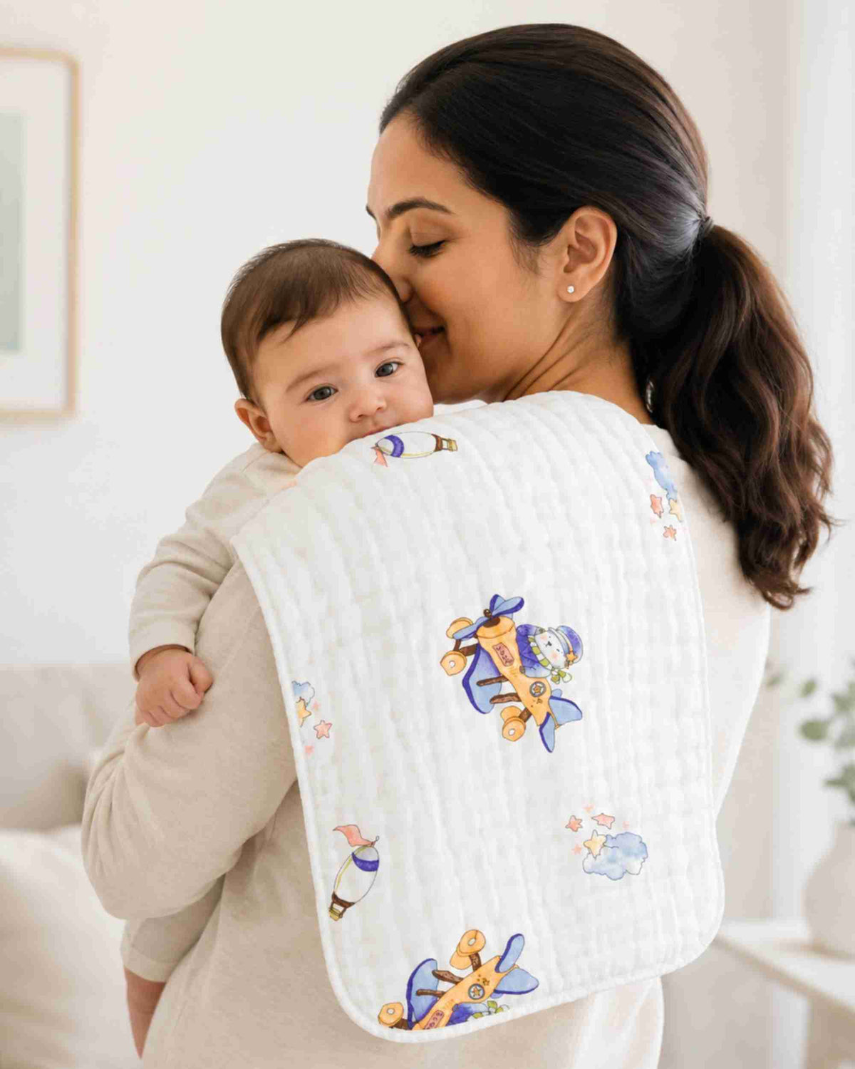 White baby burp cloth with blue airplane print, held against caregiver’s shoulder