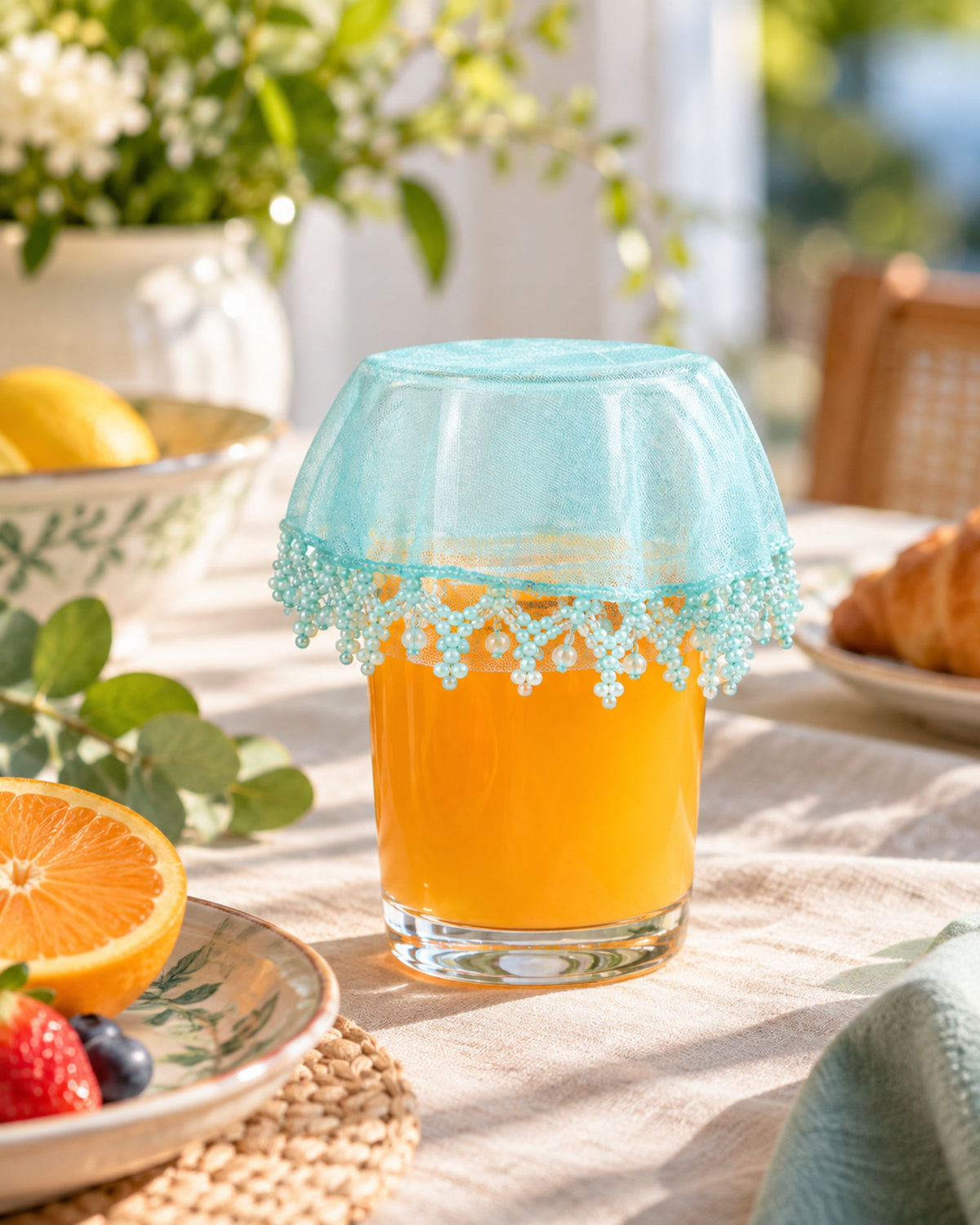 Light blue net drink glass cover with teal and white bead fringe over a drink