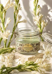 Green glass jar candle with metal latch lid and printed label, flowers nearby