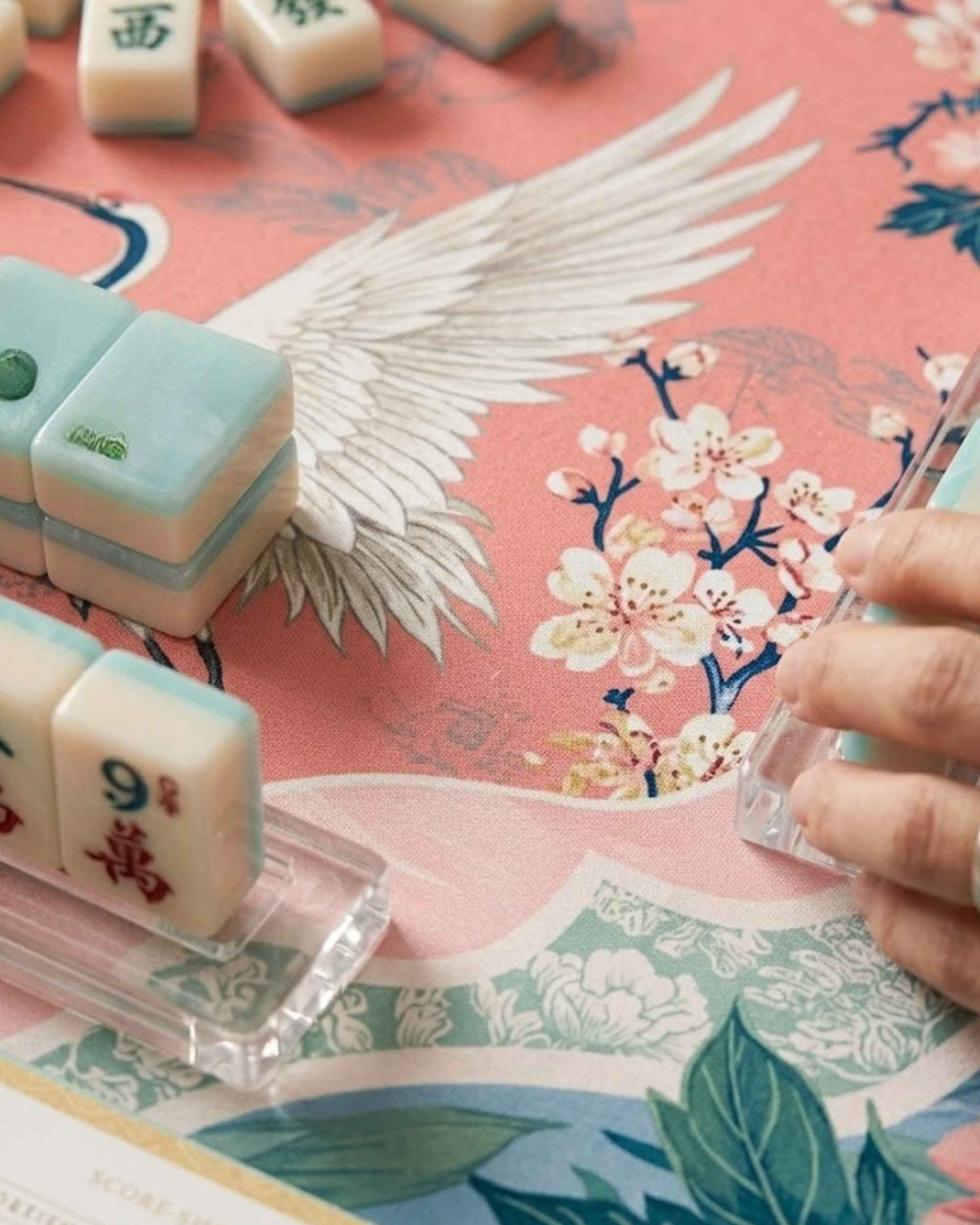 Square game mat close-up with pink cranes and floral details, with Mahjong tiles in play