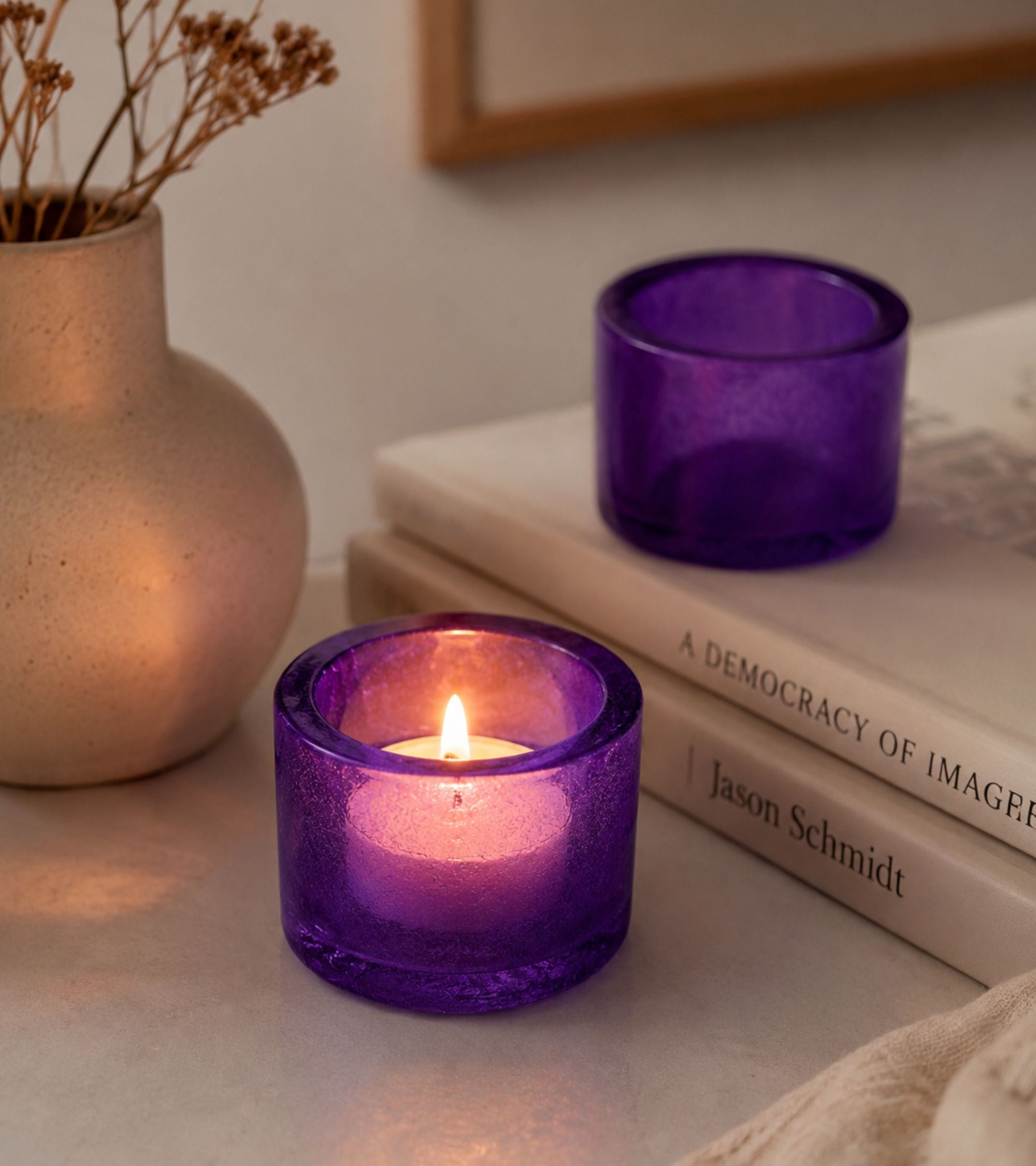 Purple glass votive candle holder with lit tealight on tabletop
