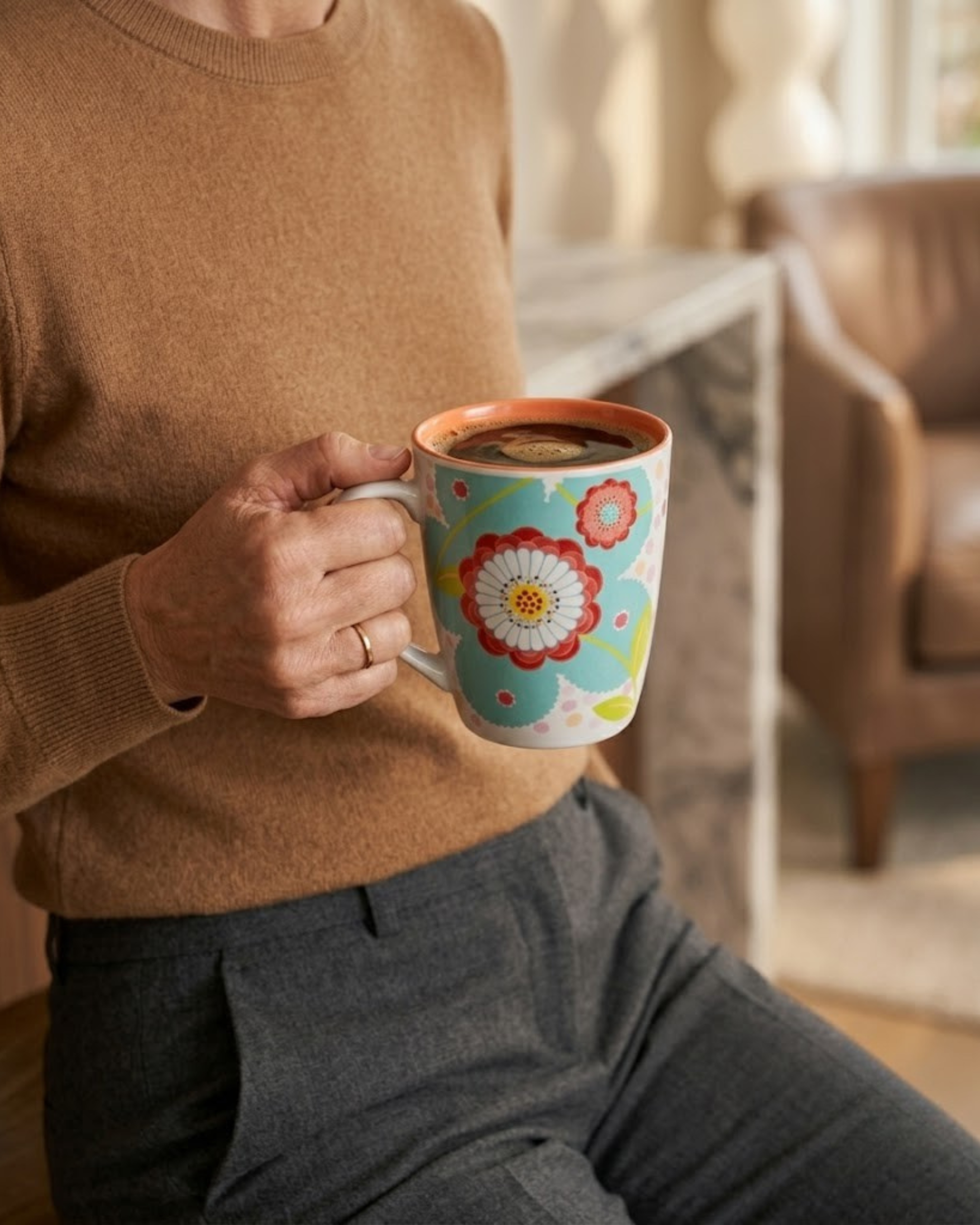 Ceramic mug with teal floral pattern, held in hand; orange interior rim visible.