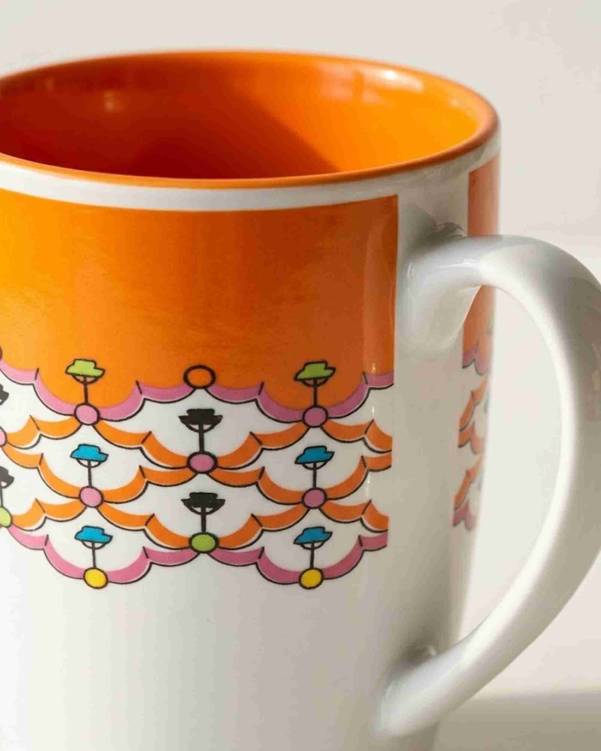 Close-up ceramic mug showing orange interior rim and colorful floral band design