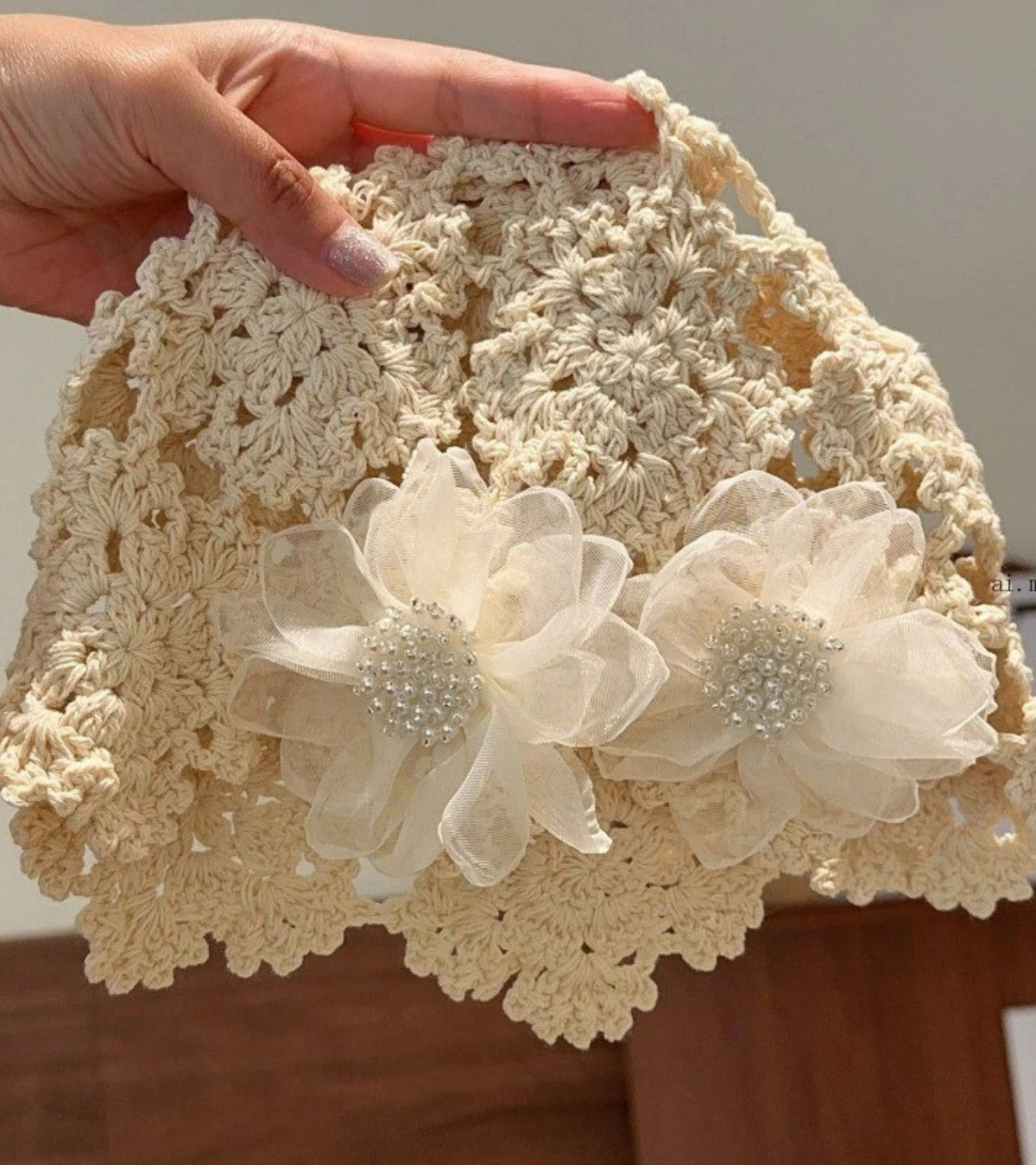 Cream crochet lace bucket cap held in hand, with organza flowers and bead details