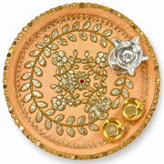 Peach round pooja thali with gold lace border, floral embroidery, and diya holders
