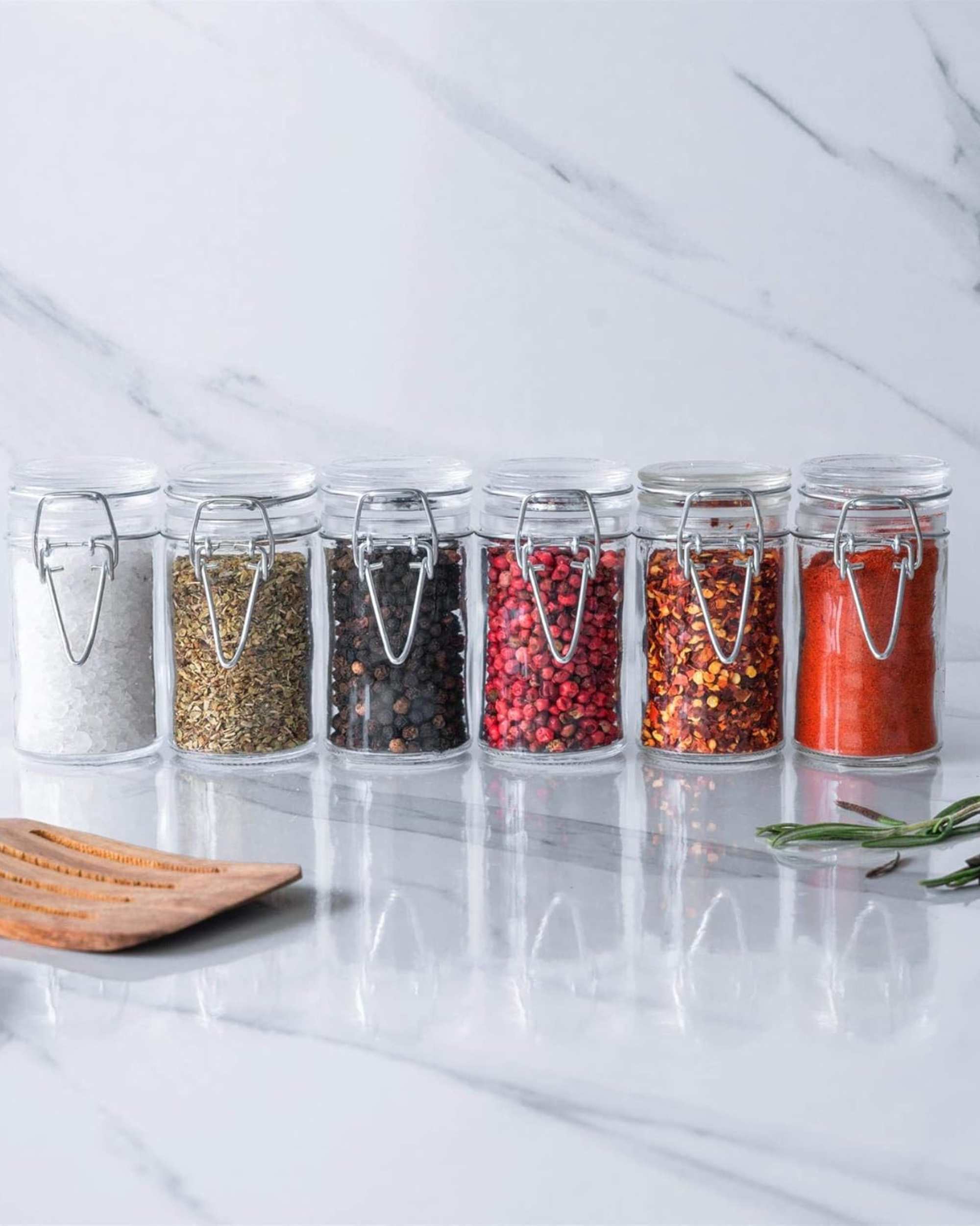 Row of clear glass clip-lock jars filled with spices and powders
