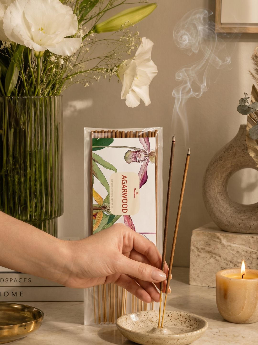 Hand placing agarwood incense sticks into a burner, next to the incense pack