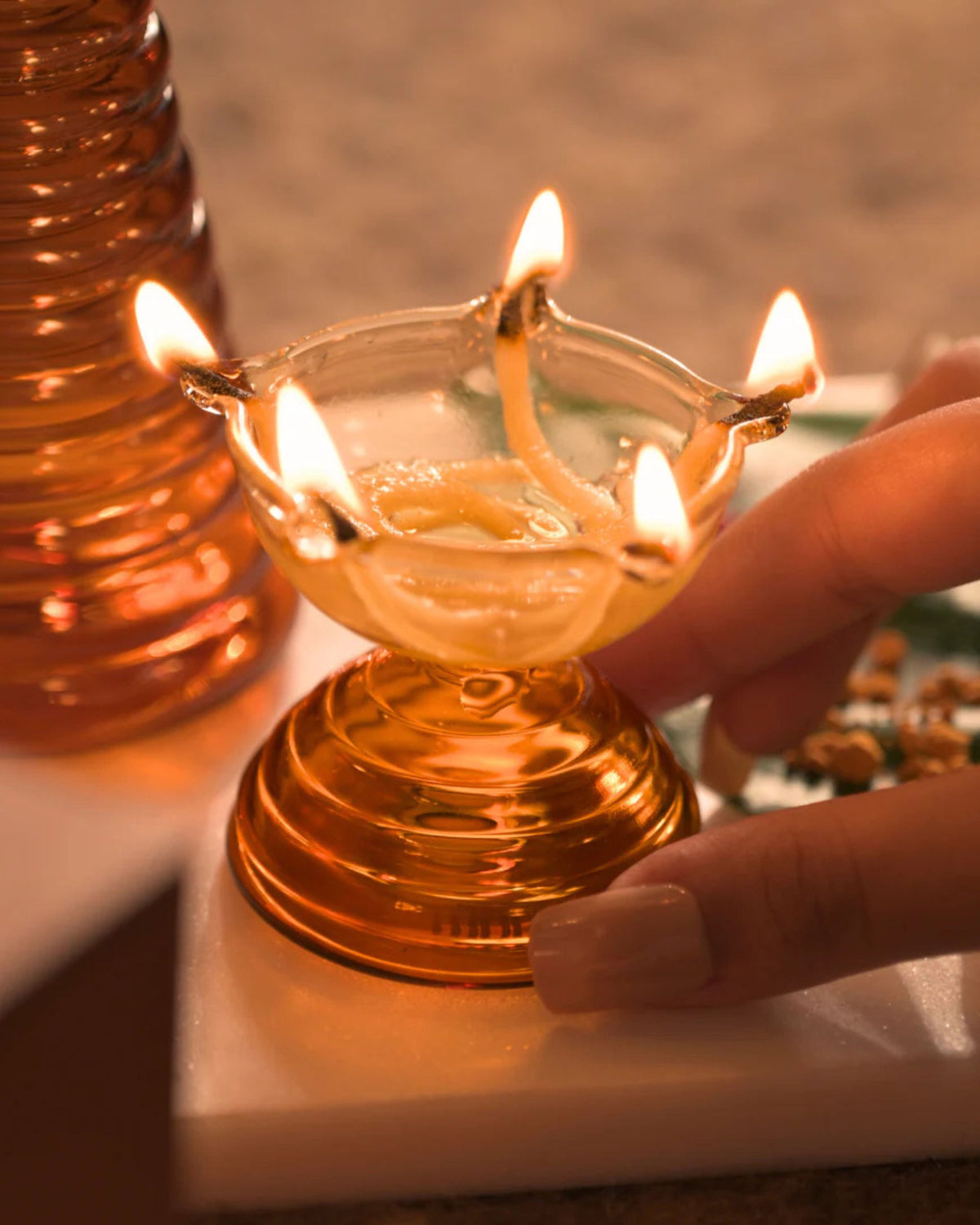 Close-up of burning clear glass puja diya bowl on amber ribbed base