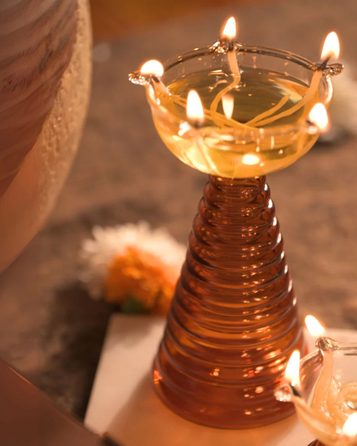 Clear glass puja diya bowl with multiple burning flames on amber ribbed stand