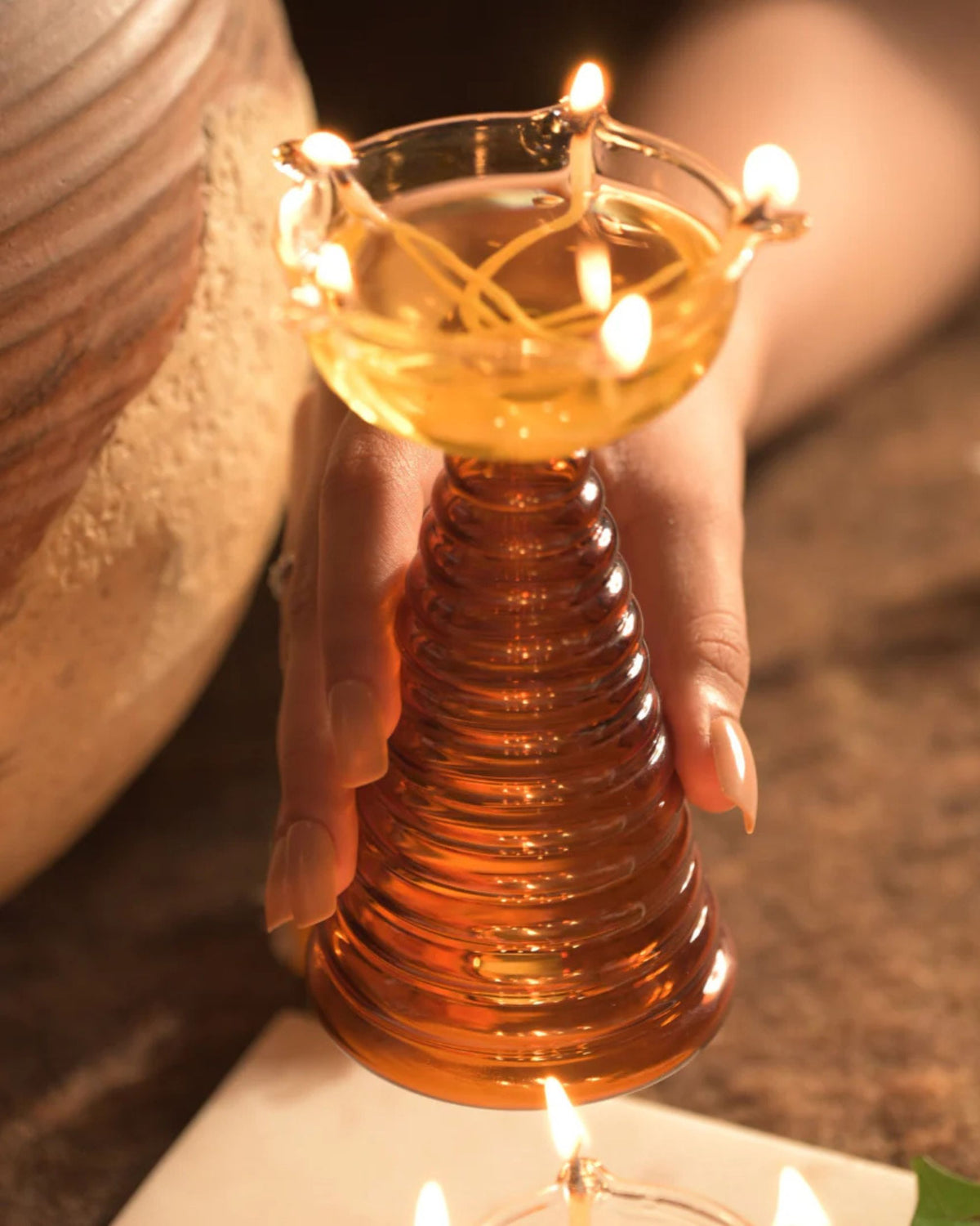 Amber ribbed glass puja diya holder with burning clear bowl, held in hand