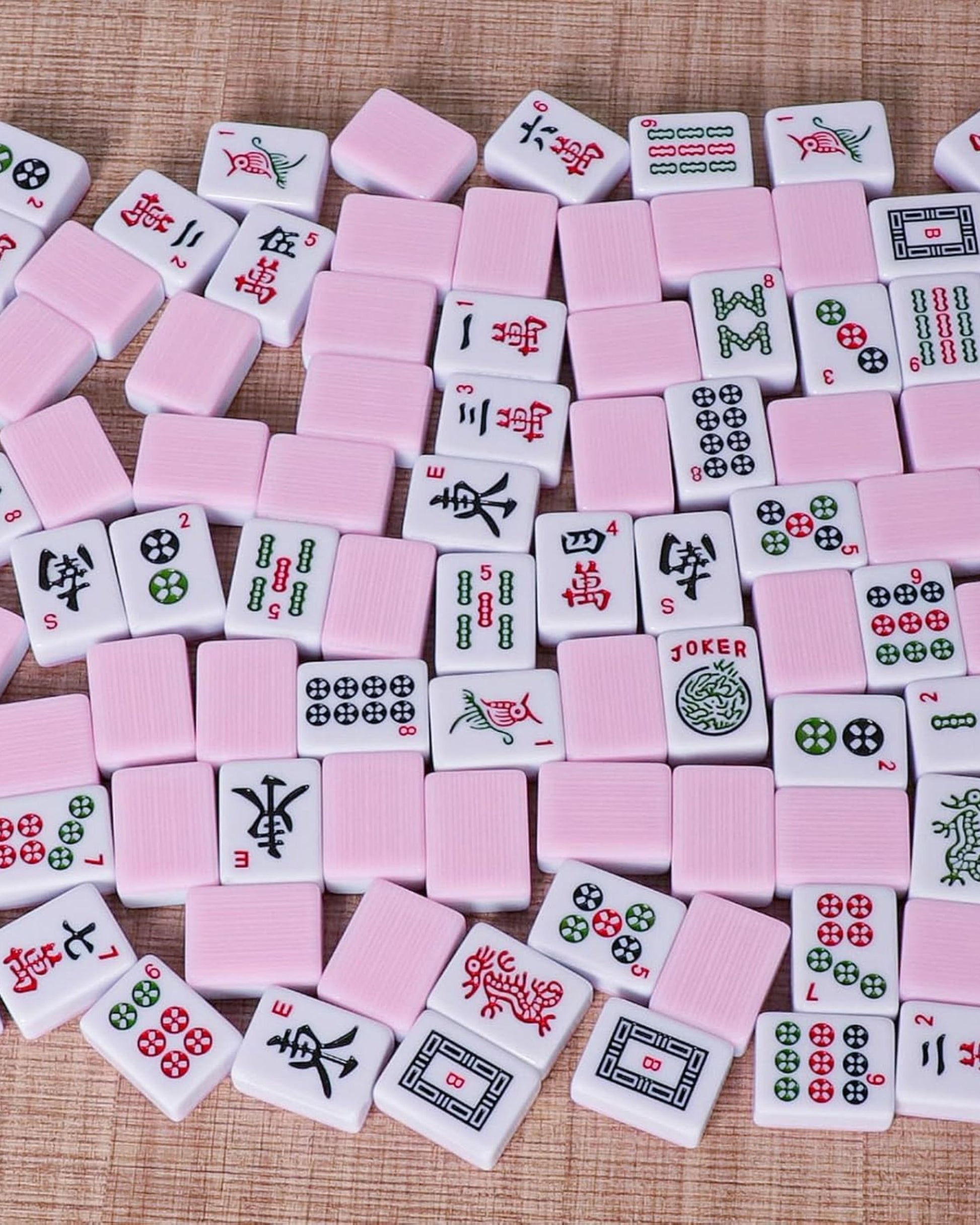 Scattered pink mahjong tiles with red, black, and green faces on a textured surface