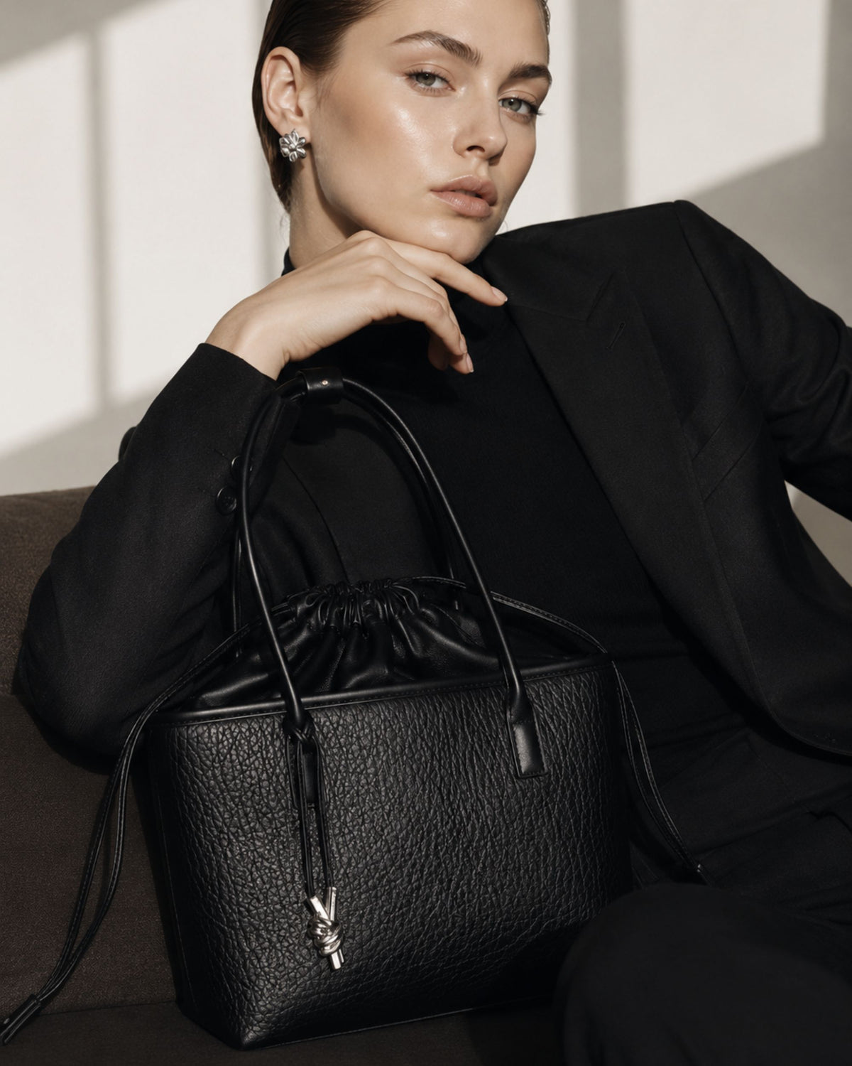 Black women's drawstring handbag with ruched top, leather handles, and key charm