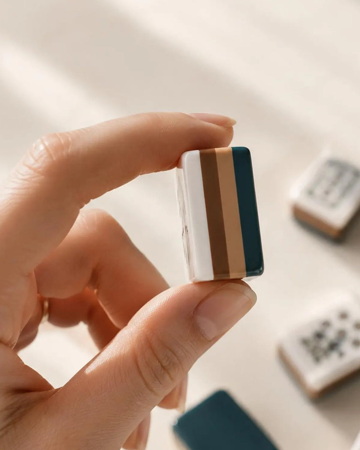 Hand holding an acrylic mahjong tile with a blue-and-brown striped border