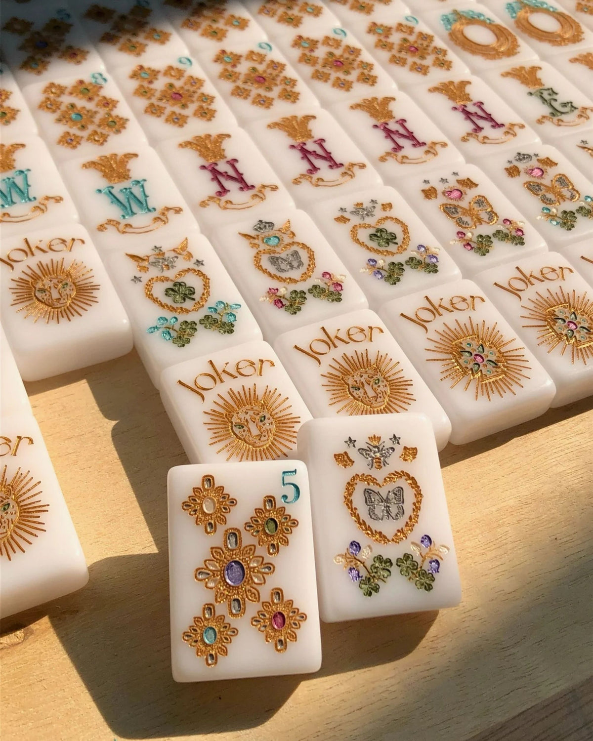 Pearlescent mahjong tiles close-up with gold flower motifs and Joker number designs