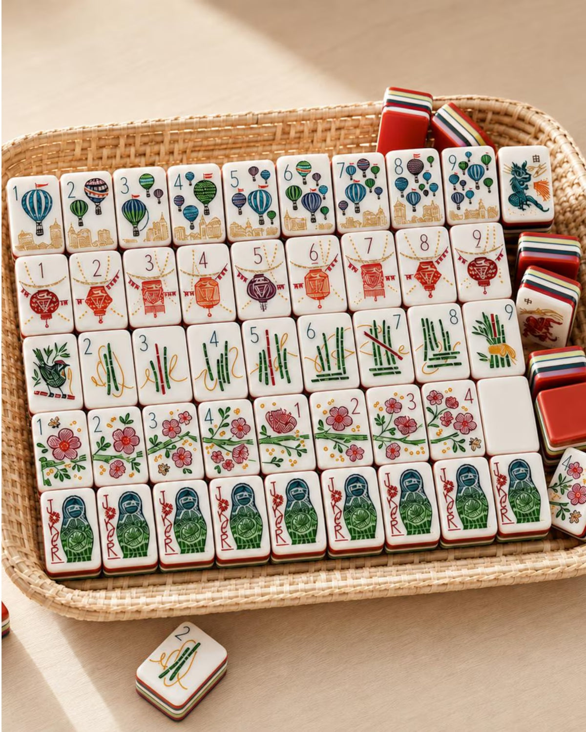 Mahjong tiles with colorful suit designs inside a woven tray; stacked tiles included
