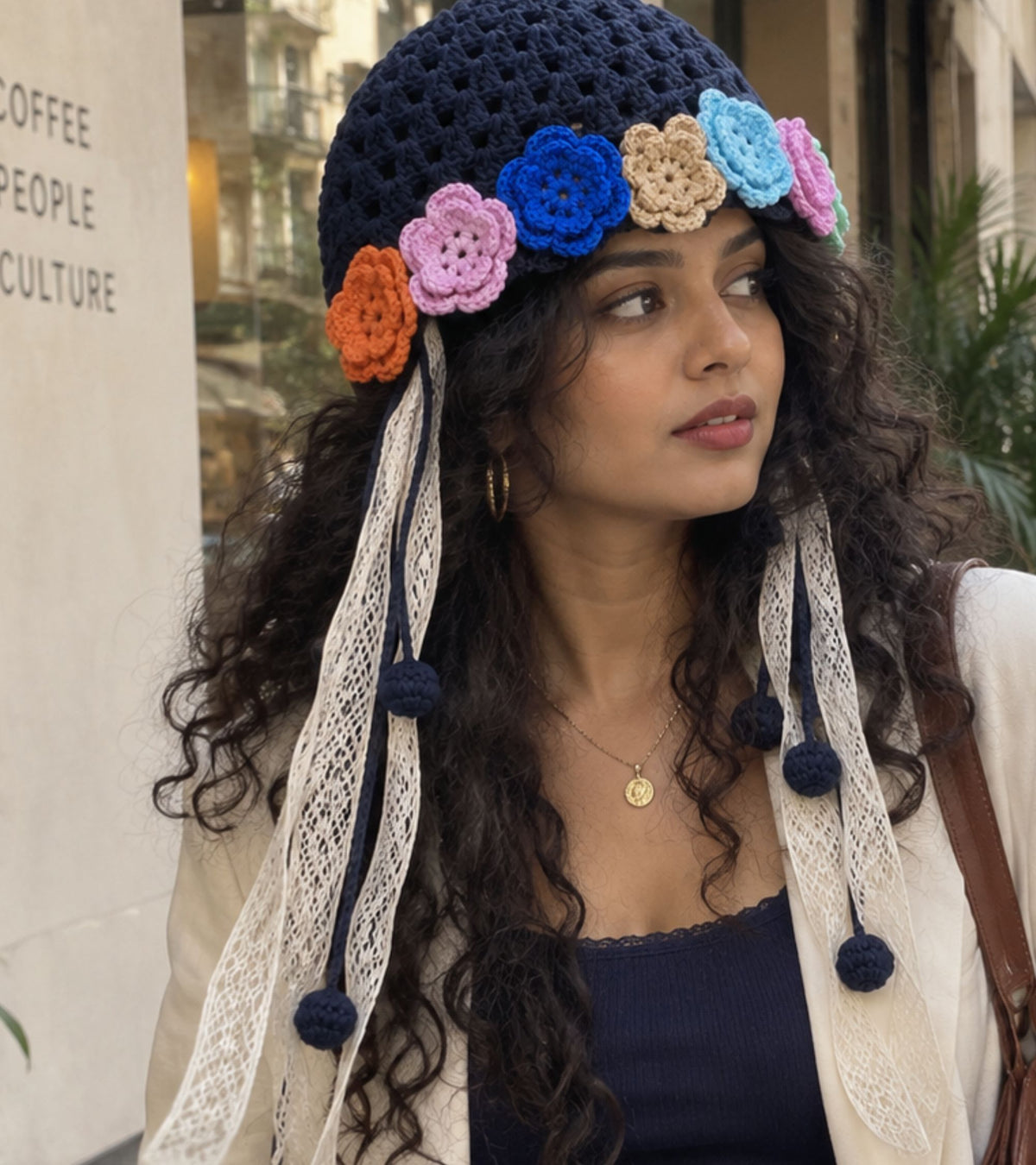 Close-up navy crochet bonnet with colorful 3D flower appliques and lace pom-pom tie ribbons