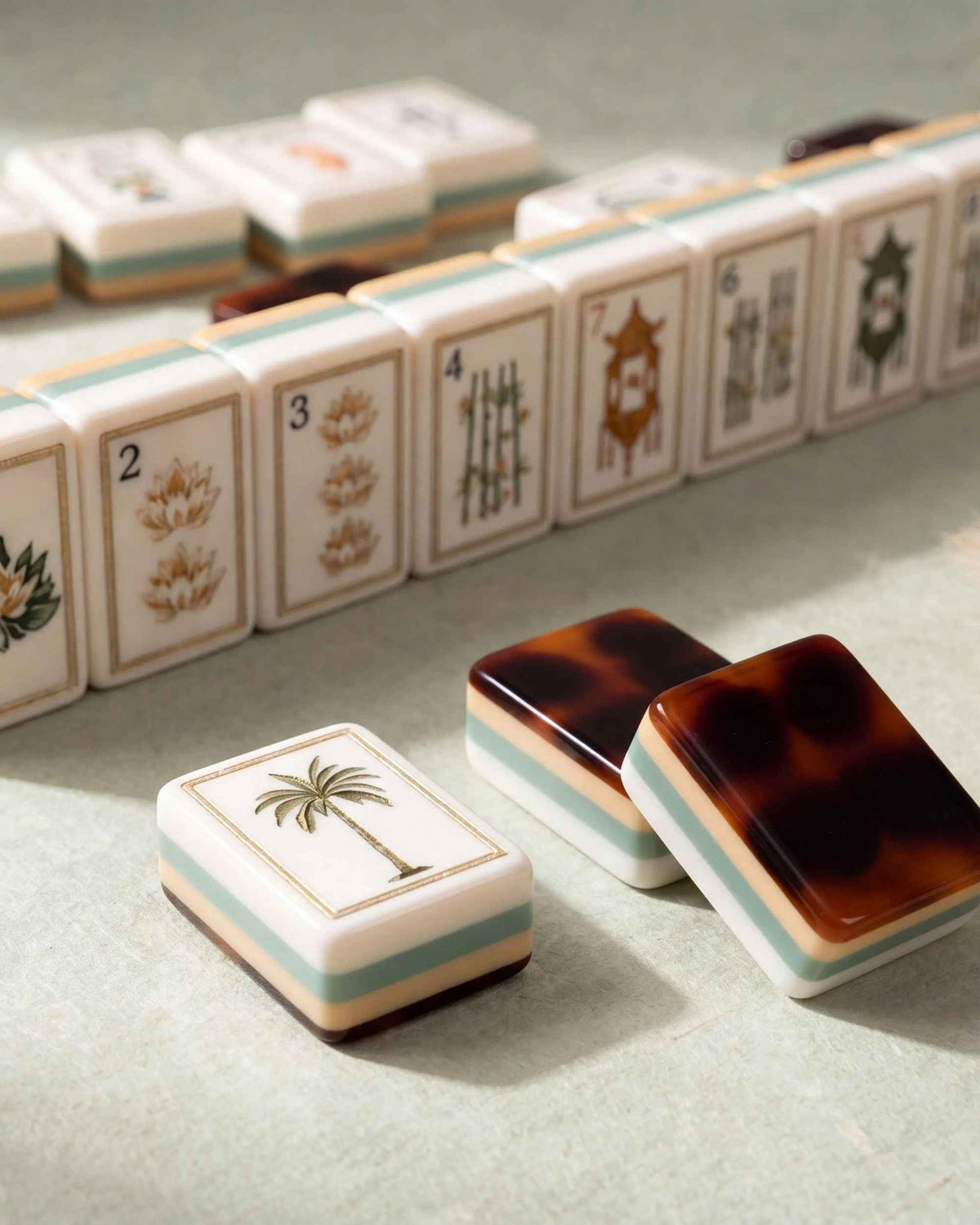 Mahjong tiles with illustrated faces; palm tree tile and tortoise-shell backs on surface.