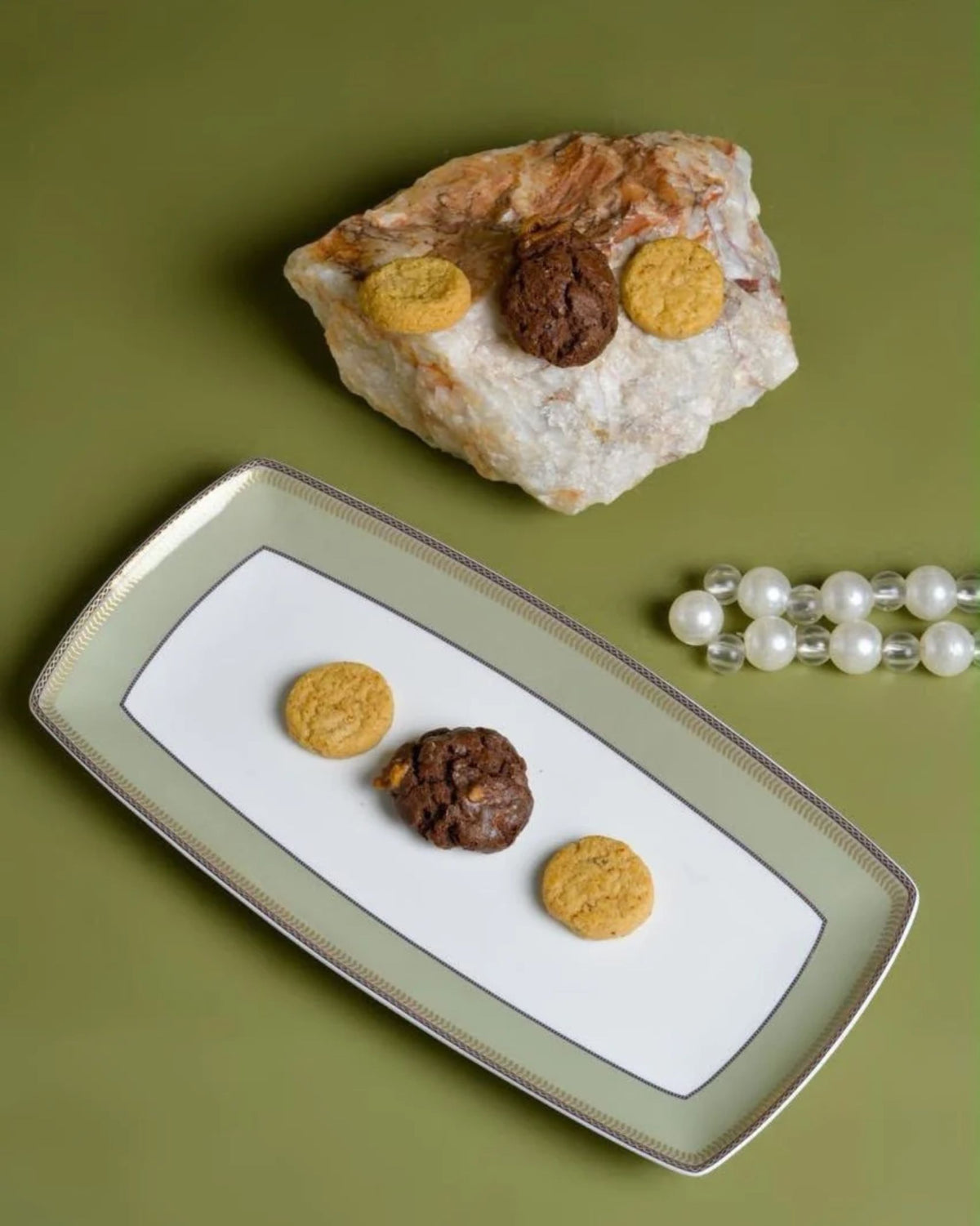 Rectangular porcelain serving plate with sage green and gold border, shown with cookies