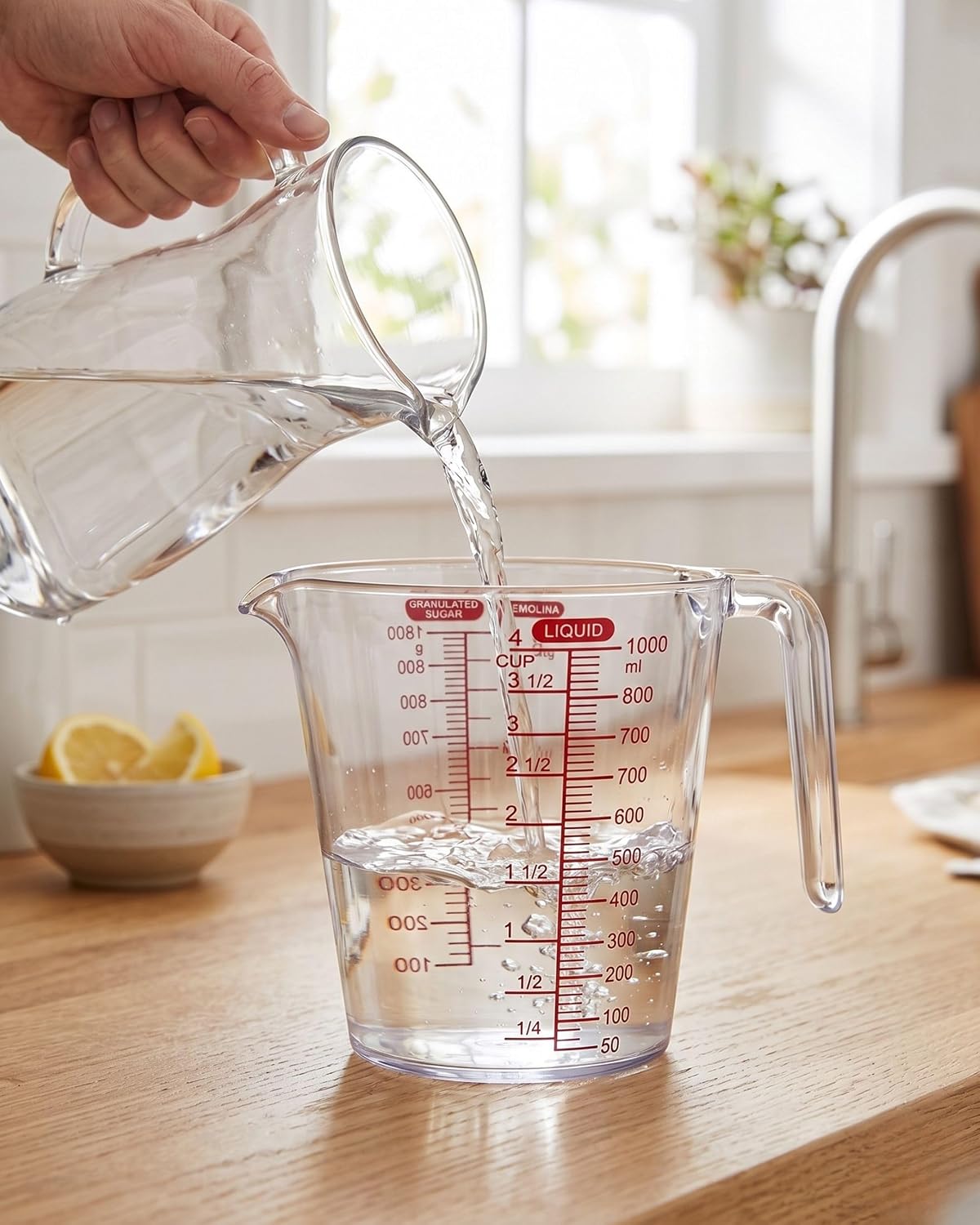 Clear measuring jug pouring liquid with red scale into another jug