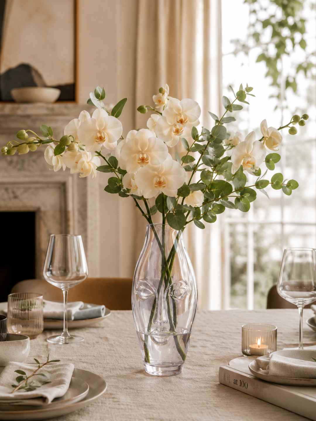 Clear glass face vase with white blossoms and green leaves on a dining table