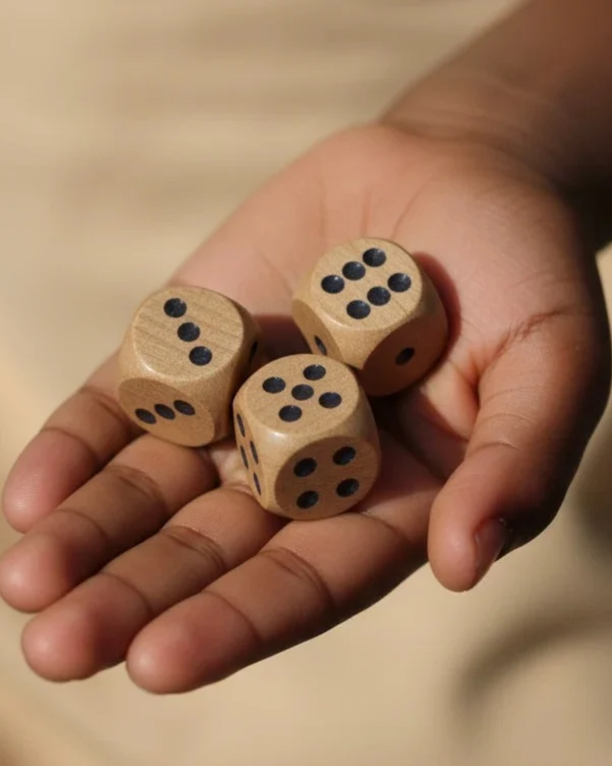 Natural wooden game dice with dot faces, held in a hand