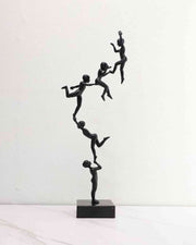 Black branch-style sculpture with stacked human figurines on square marble base