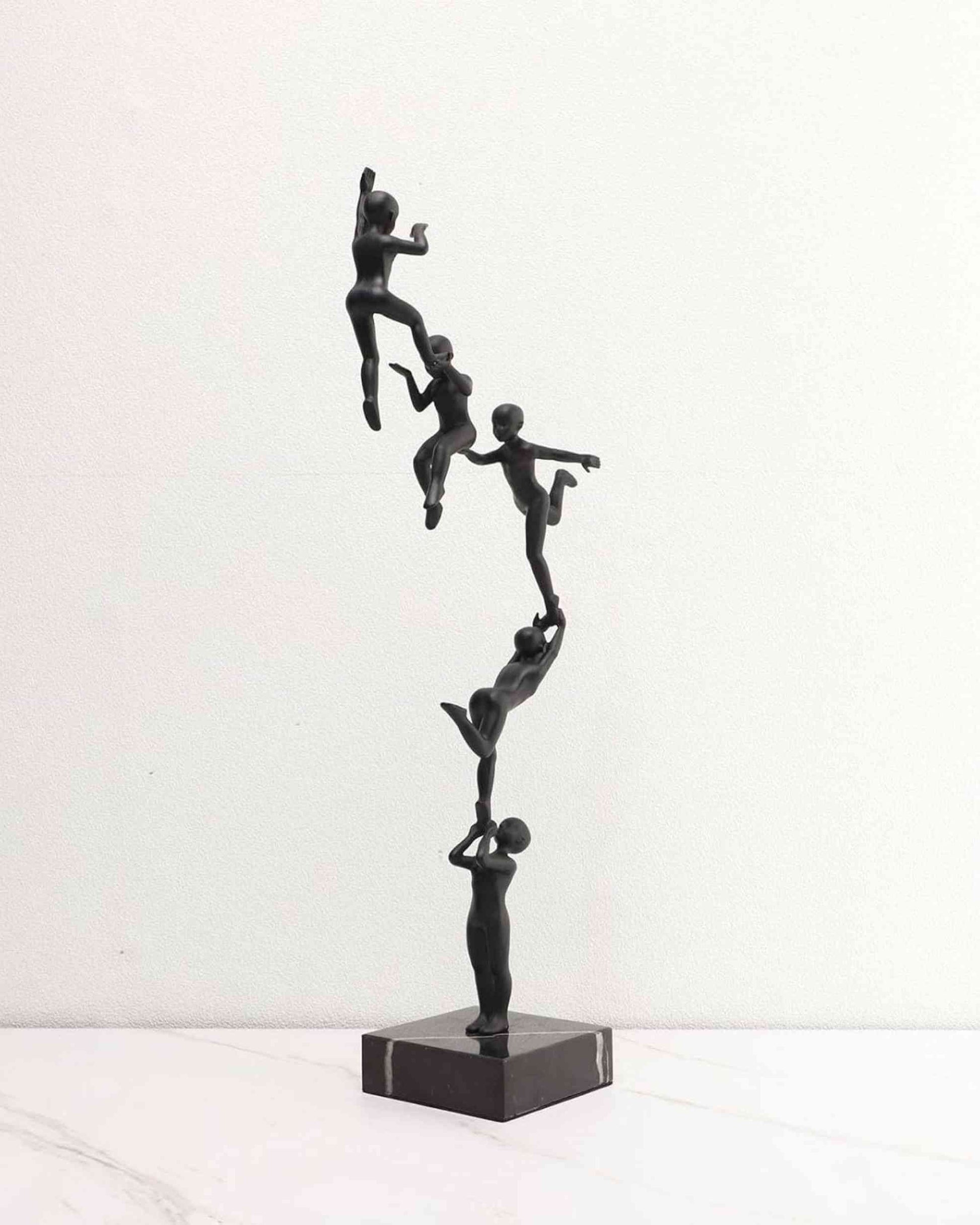 Black abstract branch sculpture with five human figurines, raised on square base