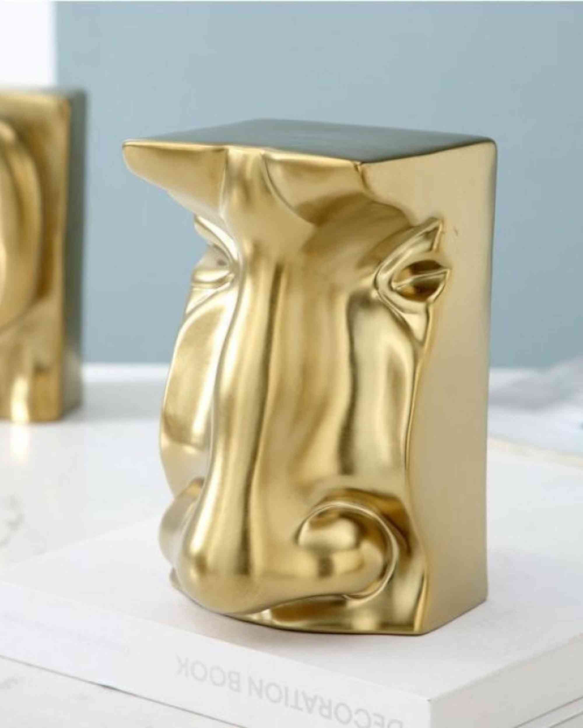 Gold resin sculptural block with embossed nose-like profile, rounded peaks