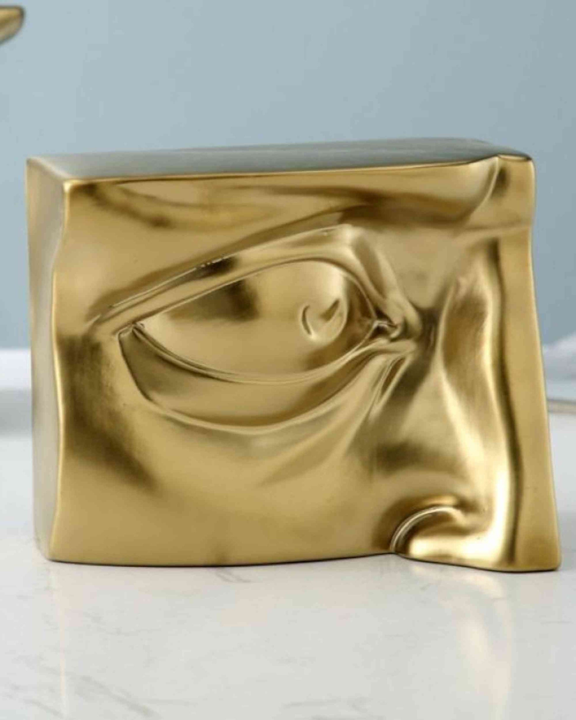 Gold resin sculptural block with embossed face profile, curved eyelid shape