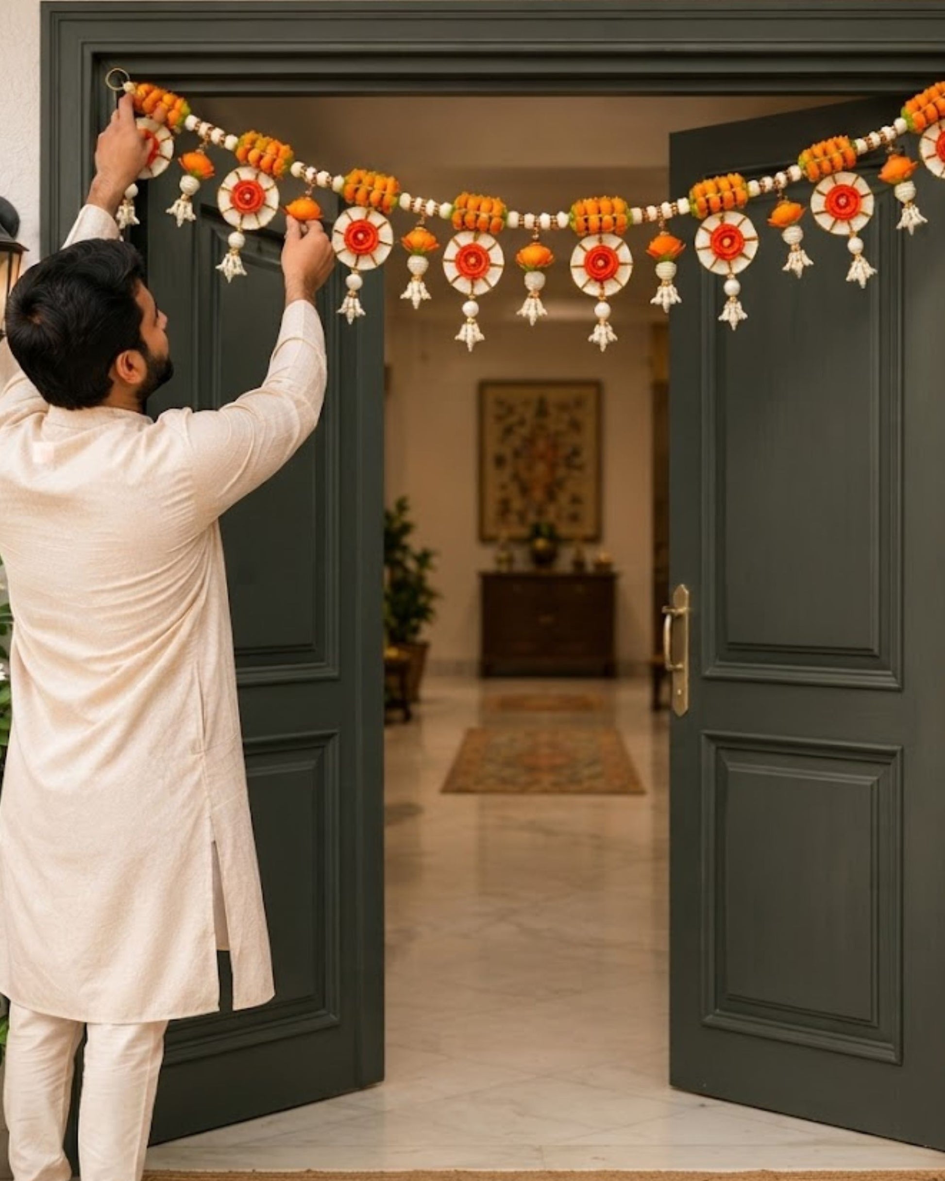 Orange floral toran garland with white pearl beads and dangling tassel ornaments on doorway
