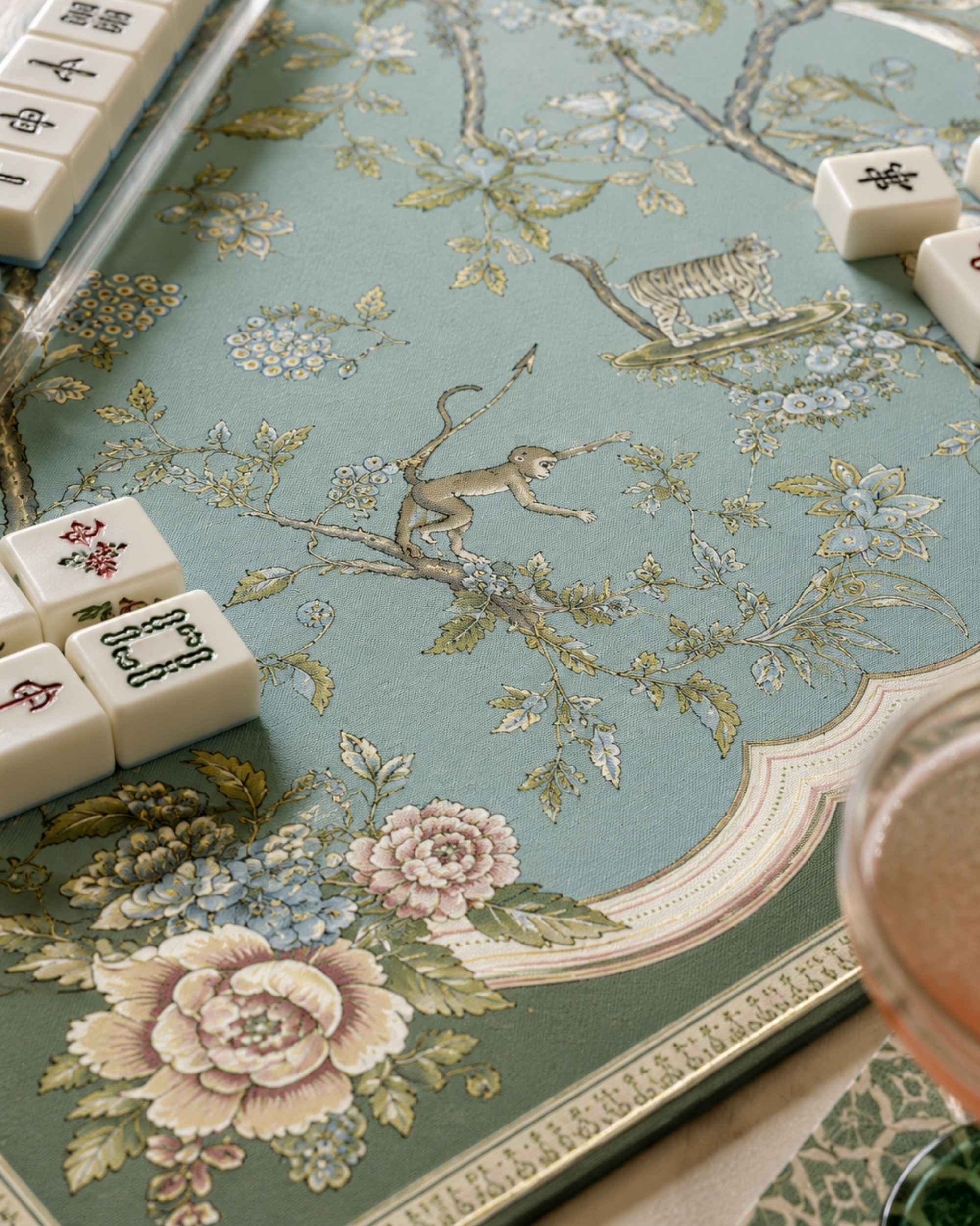 Turquoise square game mat with floral vines and bird-and-deer motif, decorative border