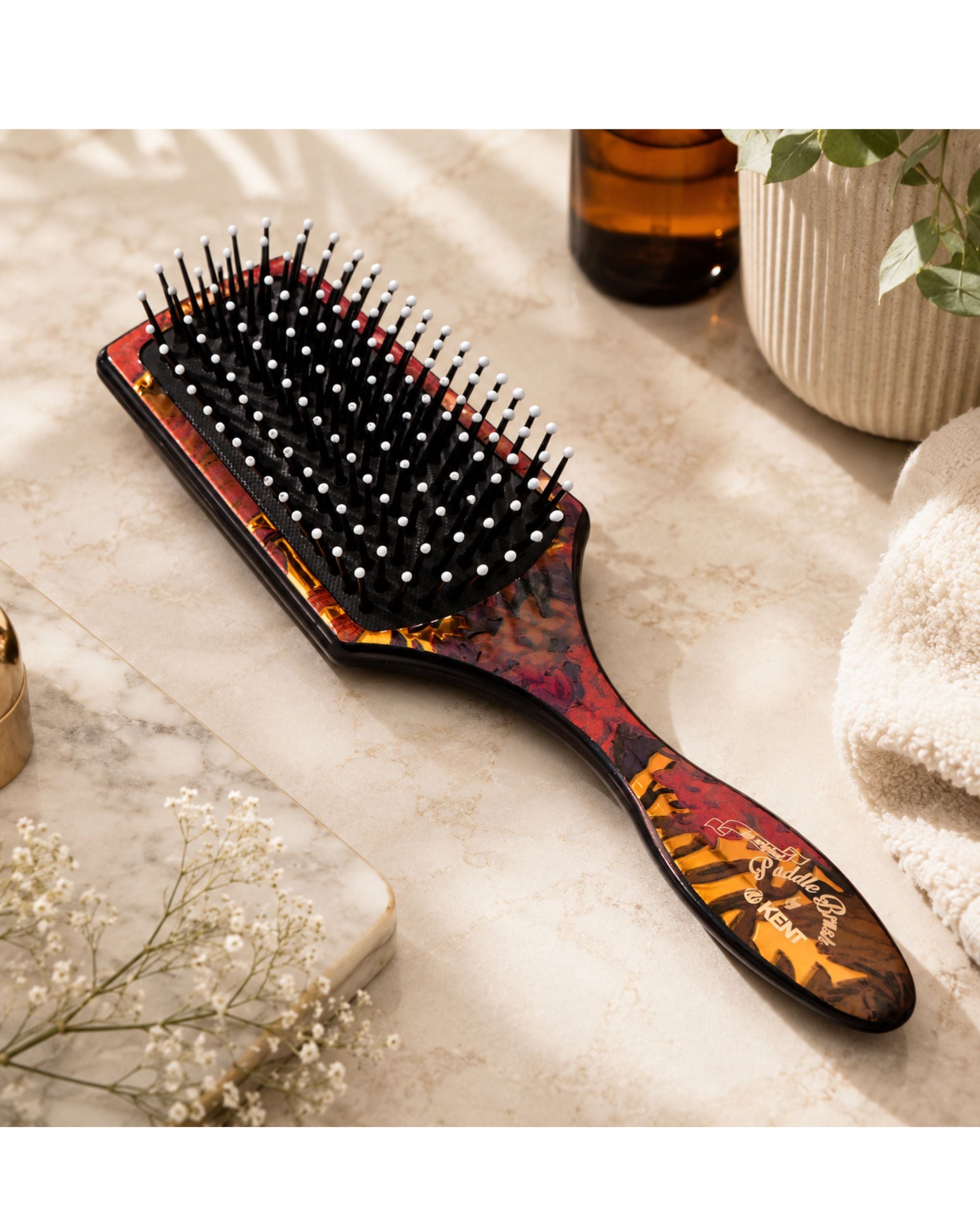 Floral paddle hair brush with black bristles and orange-brown patterned cushion