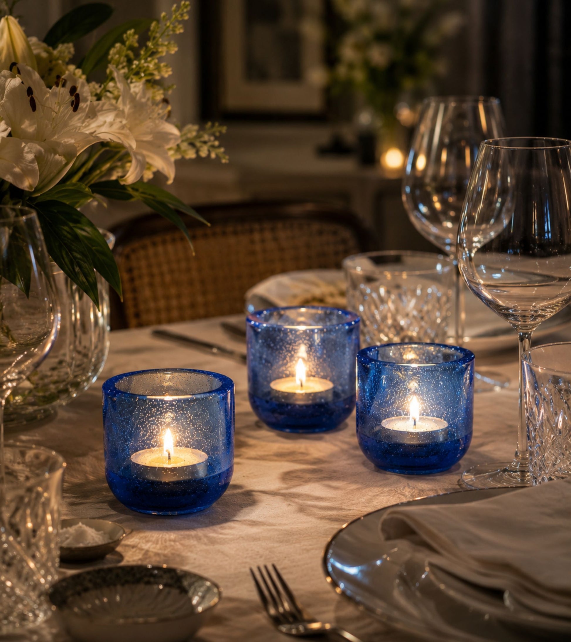 Blue glass votive candle holders with lit tealights on a table setting