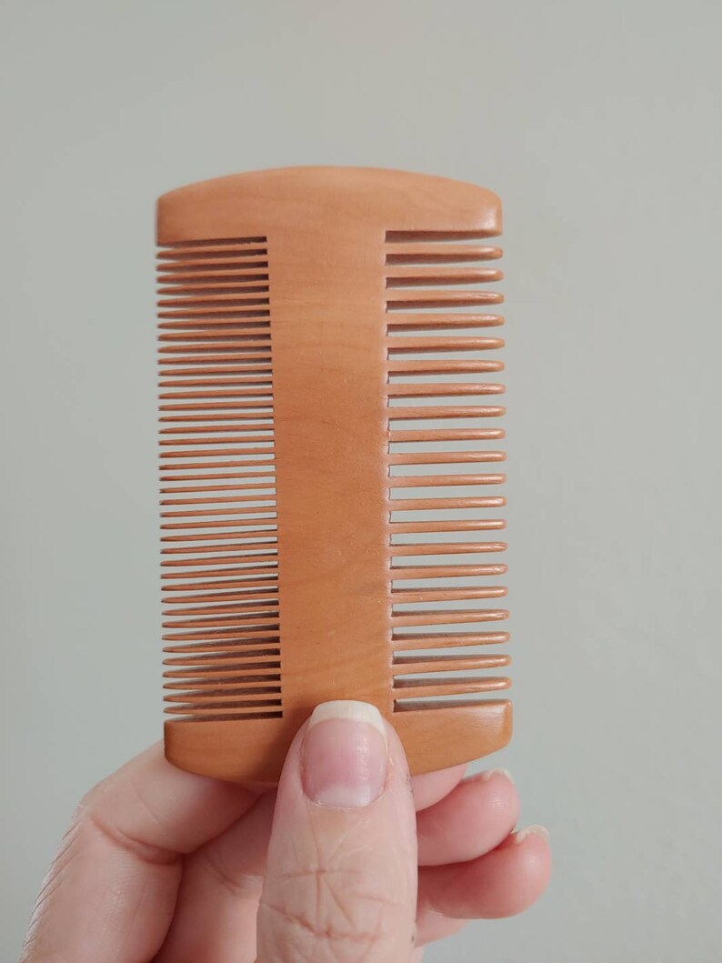 Double-sided wooden hair comb held upright, fine and wide tooth rows