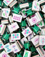 Scattered mahjong tiles with green gem frames, pink flower designs, and Joker tiles