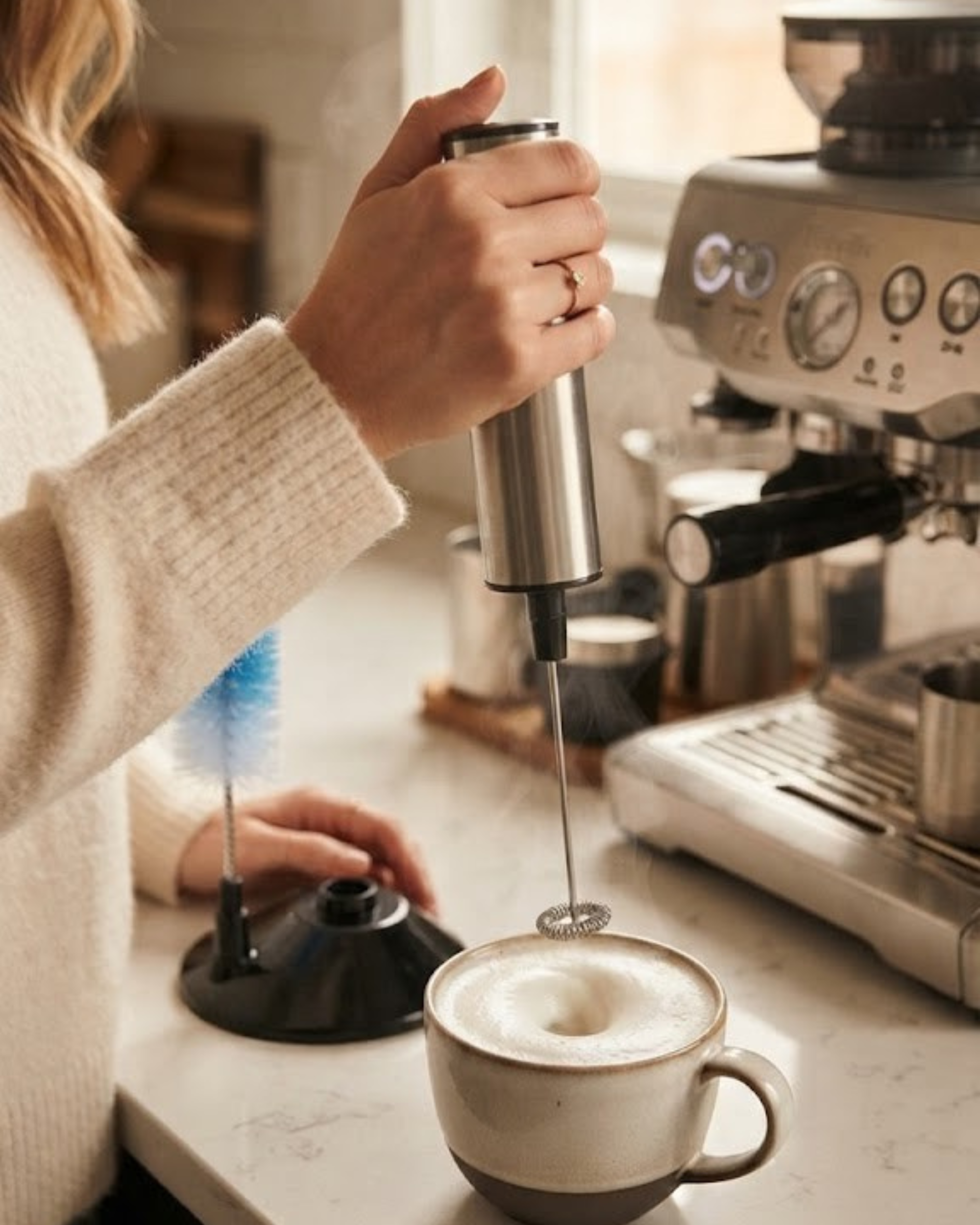 Stainless steel electric milk frother with stand, frothing wand and base.