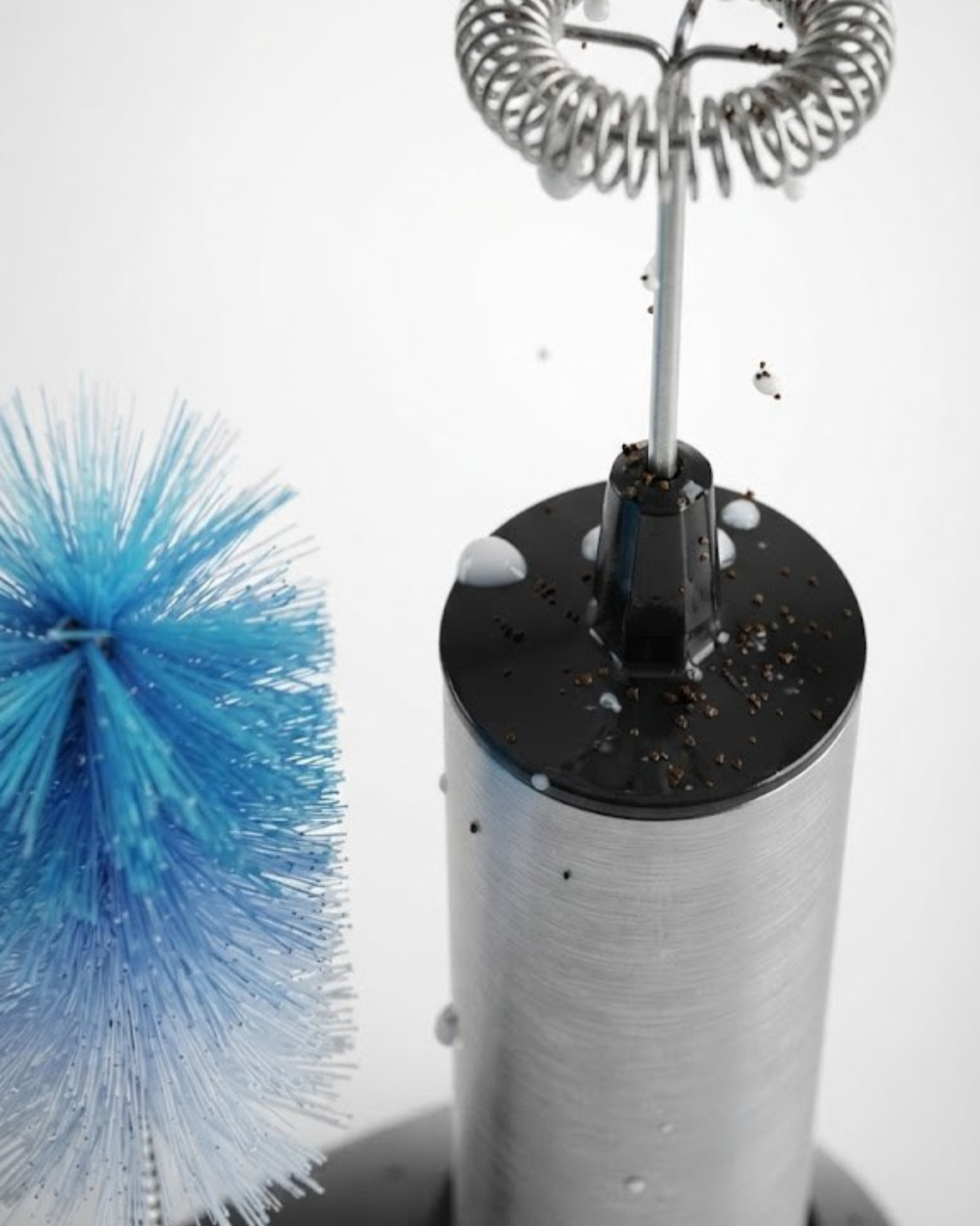 Stainless steel frother cup with whisk spring attachment and blue cleaning brush.
