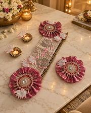 Pink and beige embroidered table runner styled on a cream marble table with glowing brass diyas and festive flowers