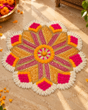 Floral rangoli mat with pink, orange, and gold embellishments, fringed edges, and a central floral motif