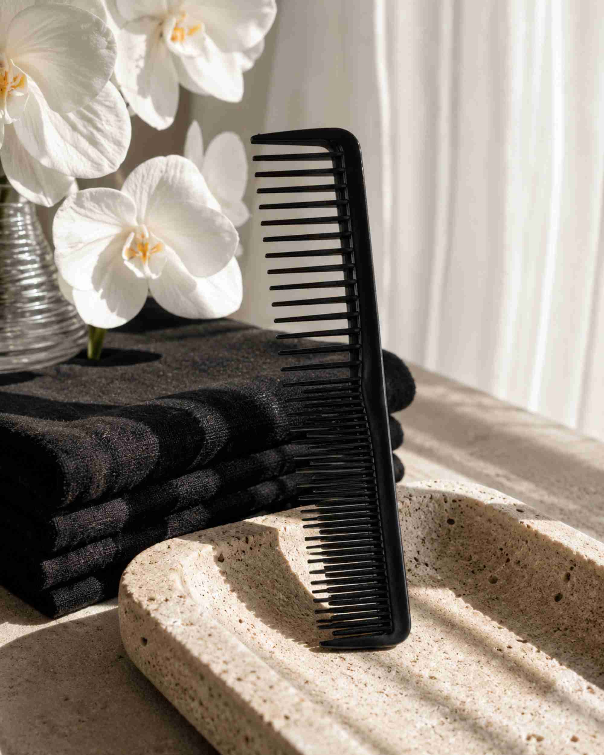Black styling comb with fine teeth and curved edge, beside a folded towel.