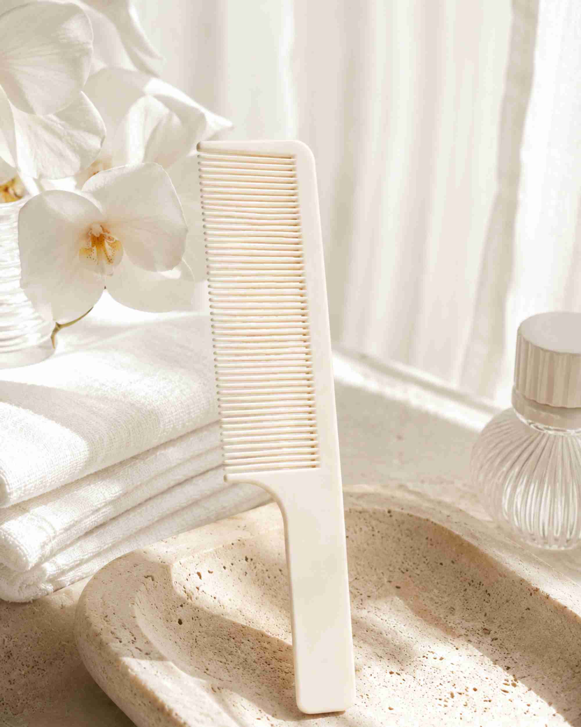 White fine-tooth handle comb placed on a bathroom sink near toiletries.